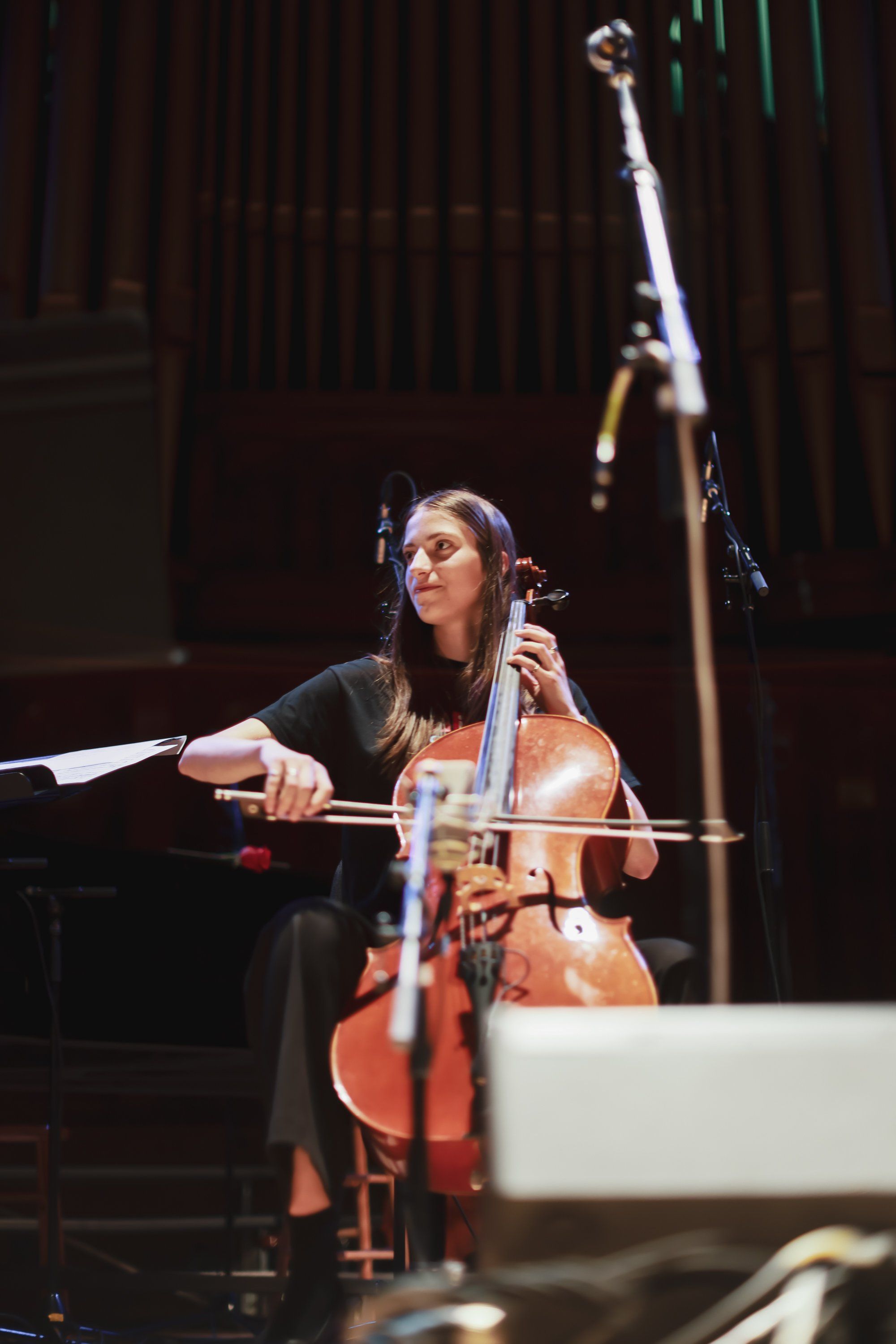 Cellist performs on stage under warm spotlight, bow raised mid-phrase, intense concentration visible on her face