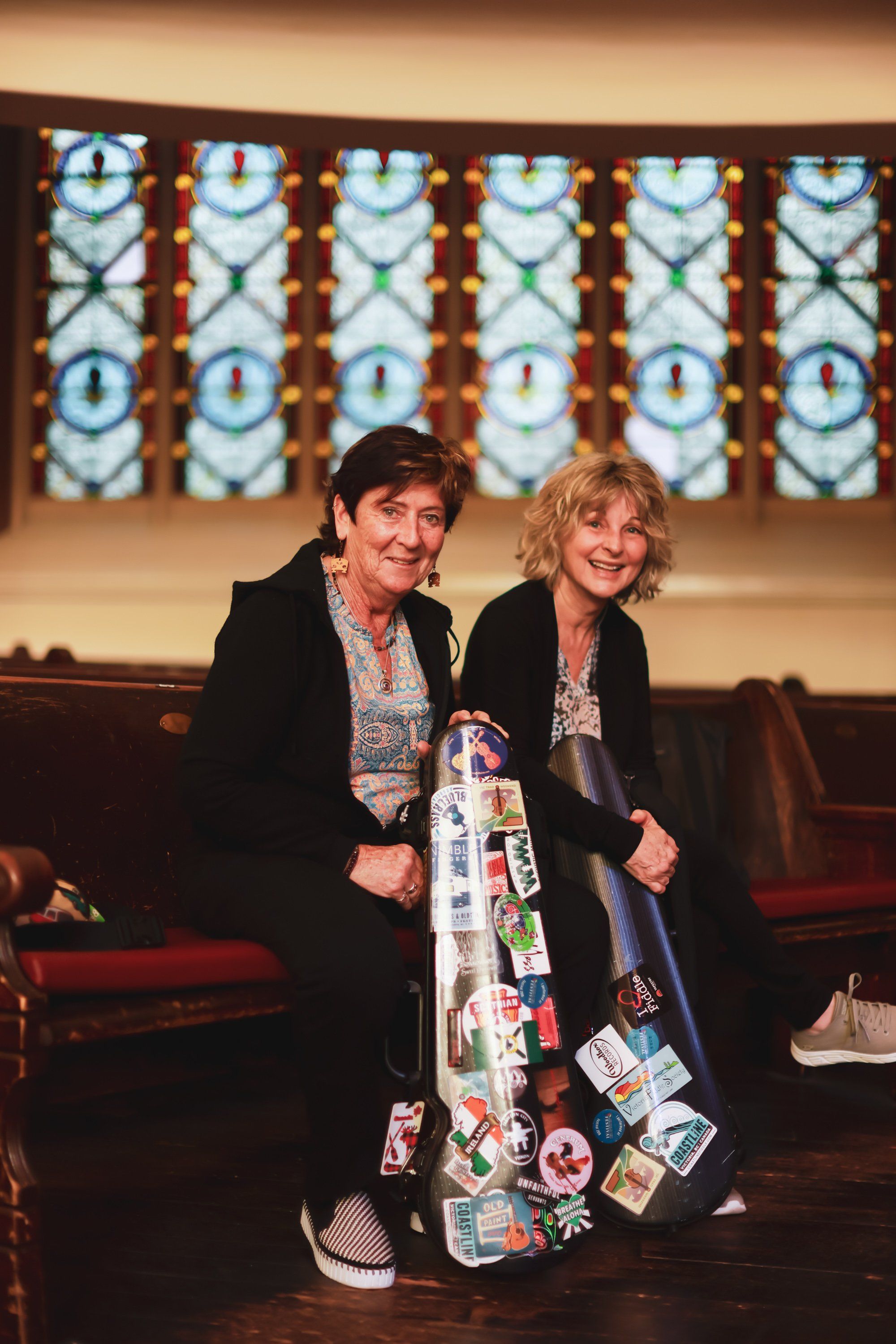 Two women sit together on a burgundy couch against an illuminated backdrop featuring geometric patterns in blue and copper tones
