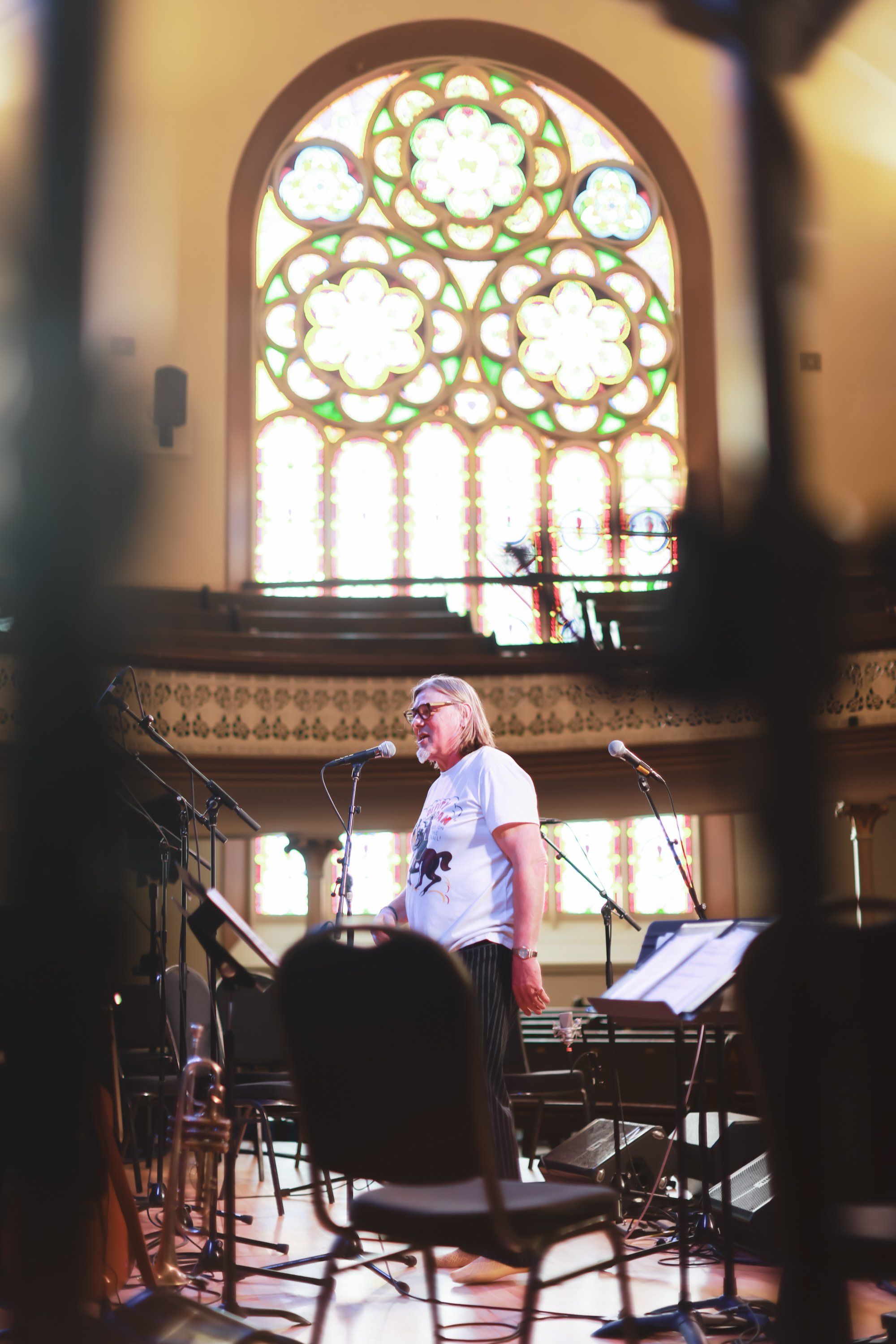 Musician performing at microphone in ornate stone chapel with luminous arched stained glass window