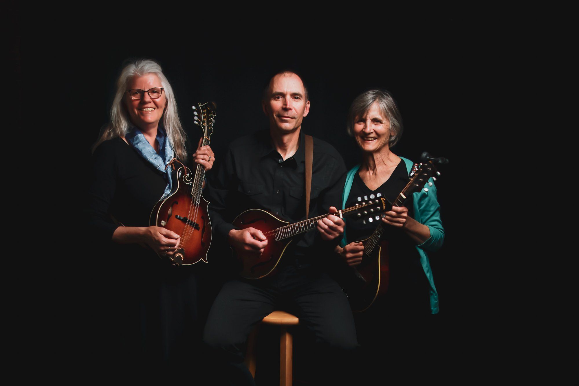 Three musicians with mandolins posed against black background, warm stage lighting illuminating their instruments and faces