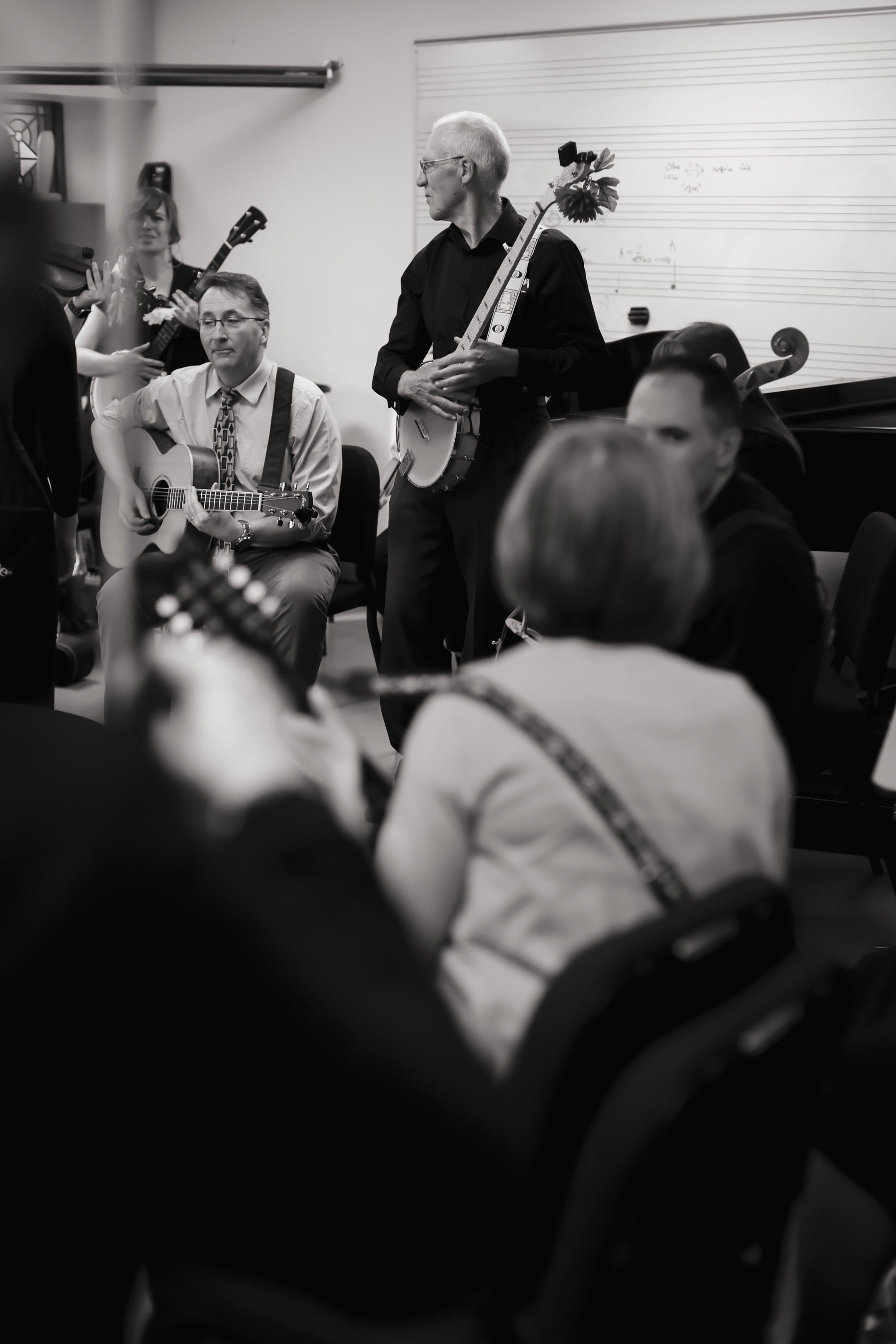 Elderly musicians perform with guitars in a black and white intimate concert setting surrounded by seated audience members