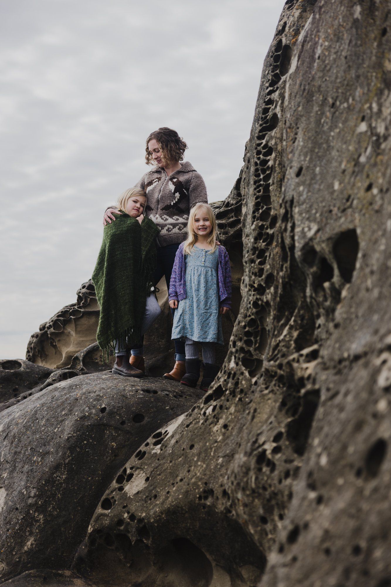 Woman and two children standing against weathered coastal rocks under overcast sky
