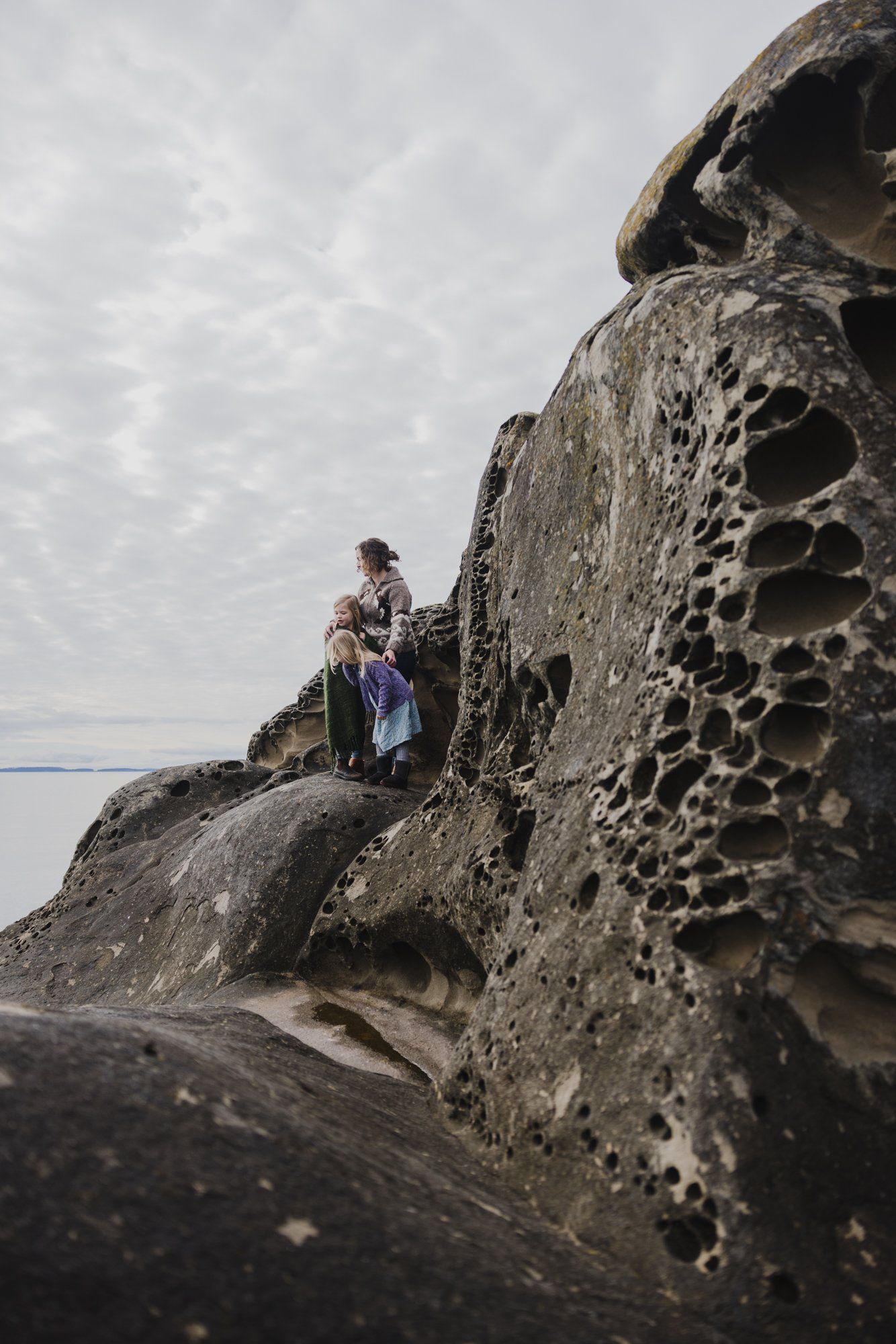 Family standing on weathered volcanic rock formations along a misty shoreline, overcast sky above