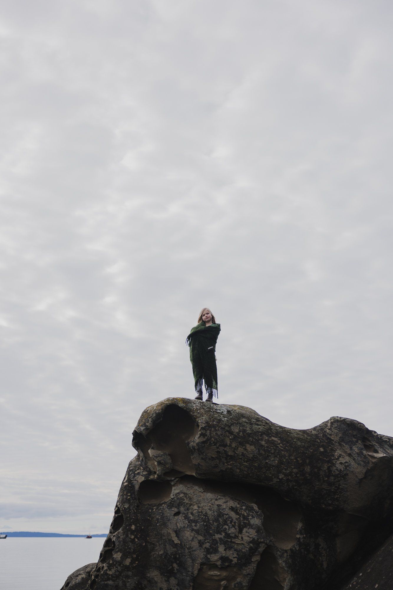 Woman standing atop a dramatic rocky outcrop under overcast skies, a blue rope visible below