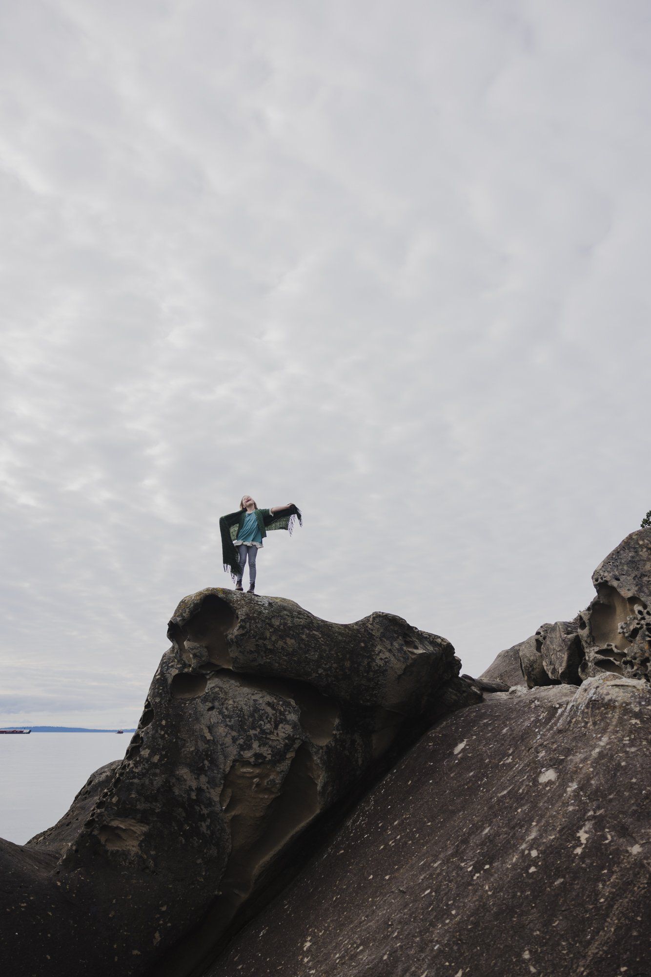 Man holding child stand on weathered rock outcrop overlooking grey water under overcast sky
