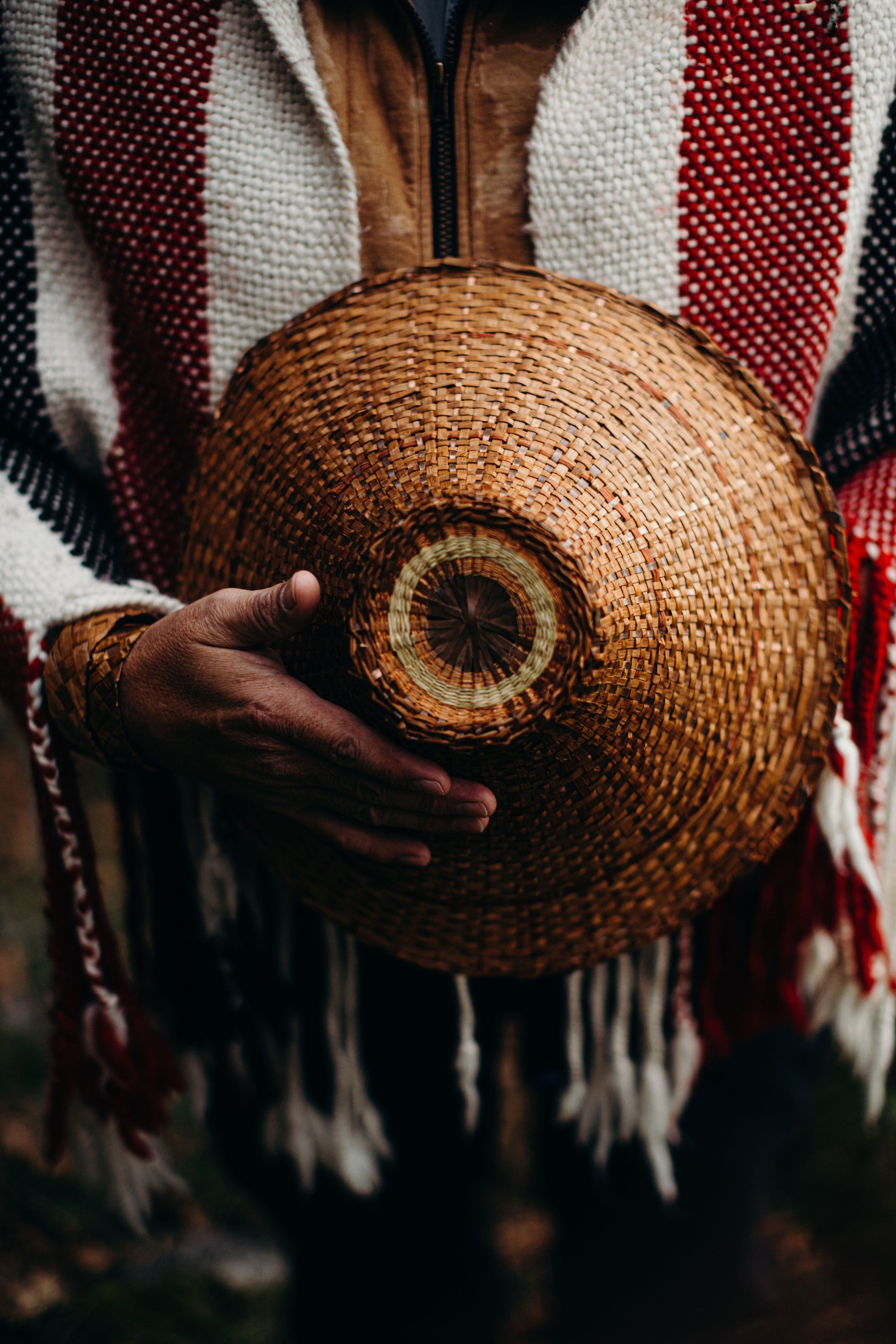 Hands holding a woven cedar basket against a striped blanket with warm, golden light illuminating the intricate weaving