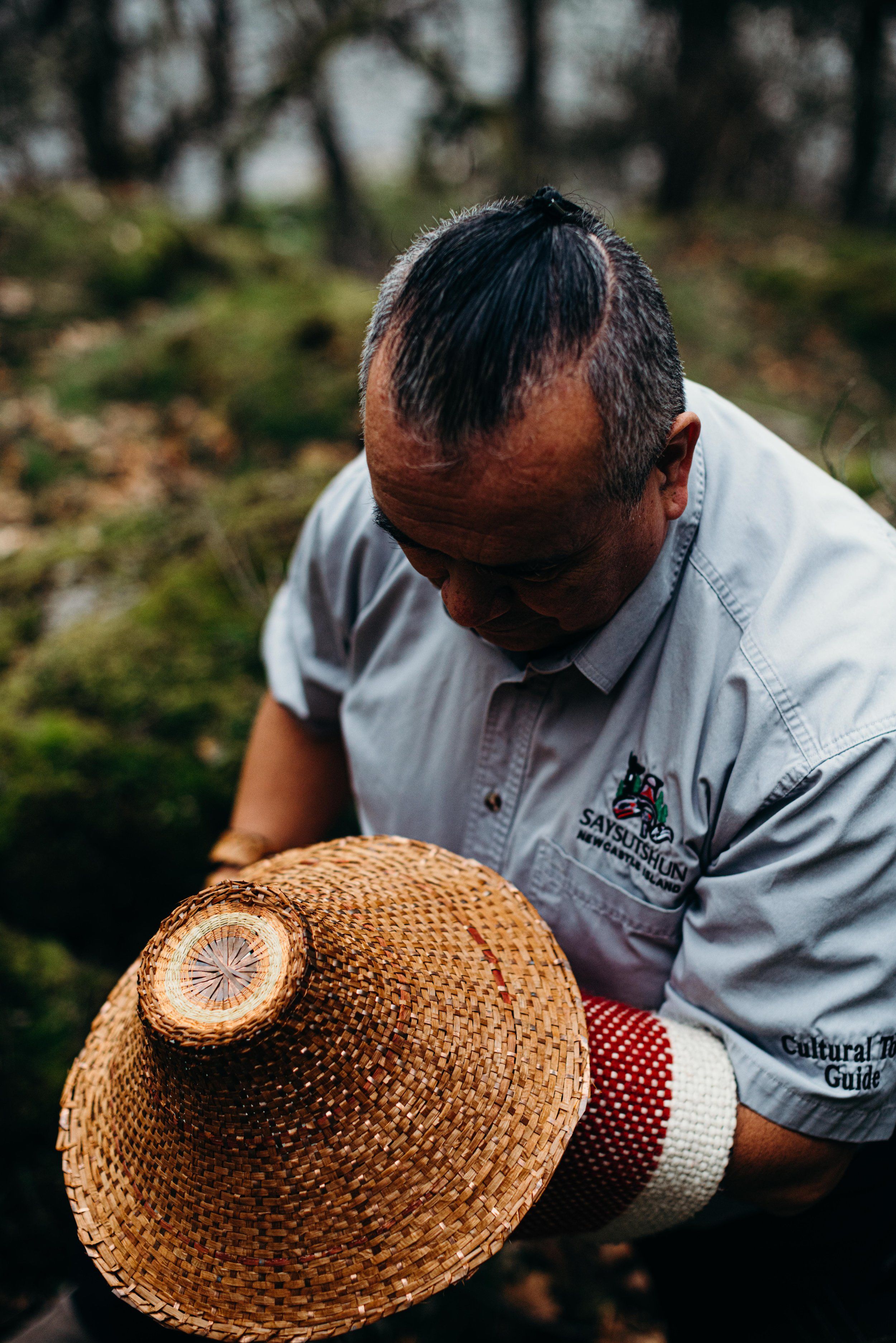 Man in light shirt examines woven basket in misty forest clearing, soft natural light illuminating weathered hands and craft detail