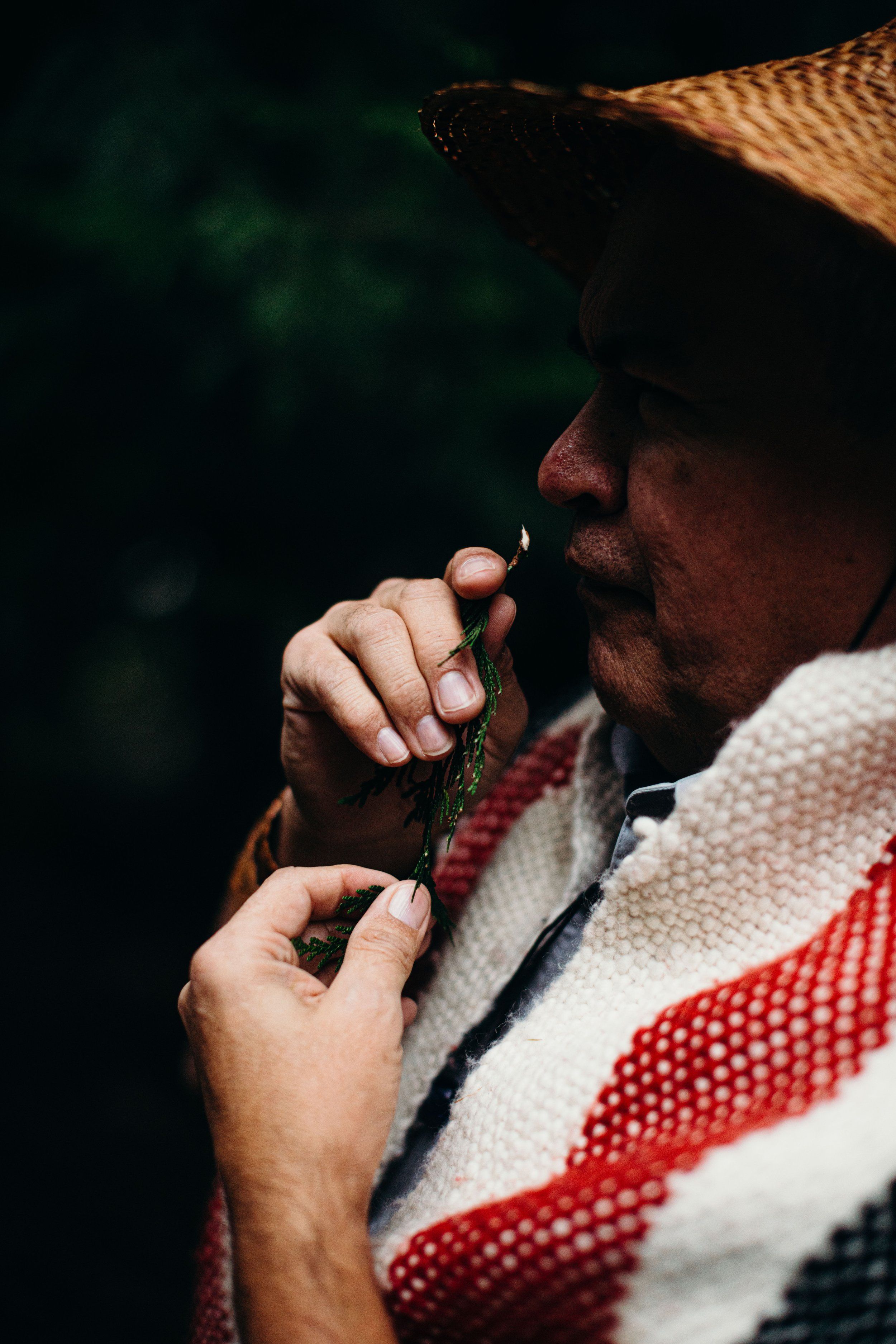 Man in straw hat and red-striped sweater holds braided rope close to his face against dark water background