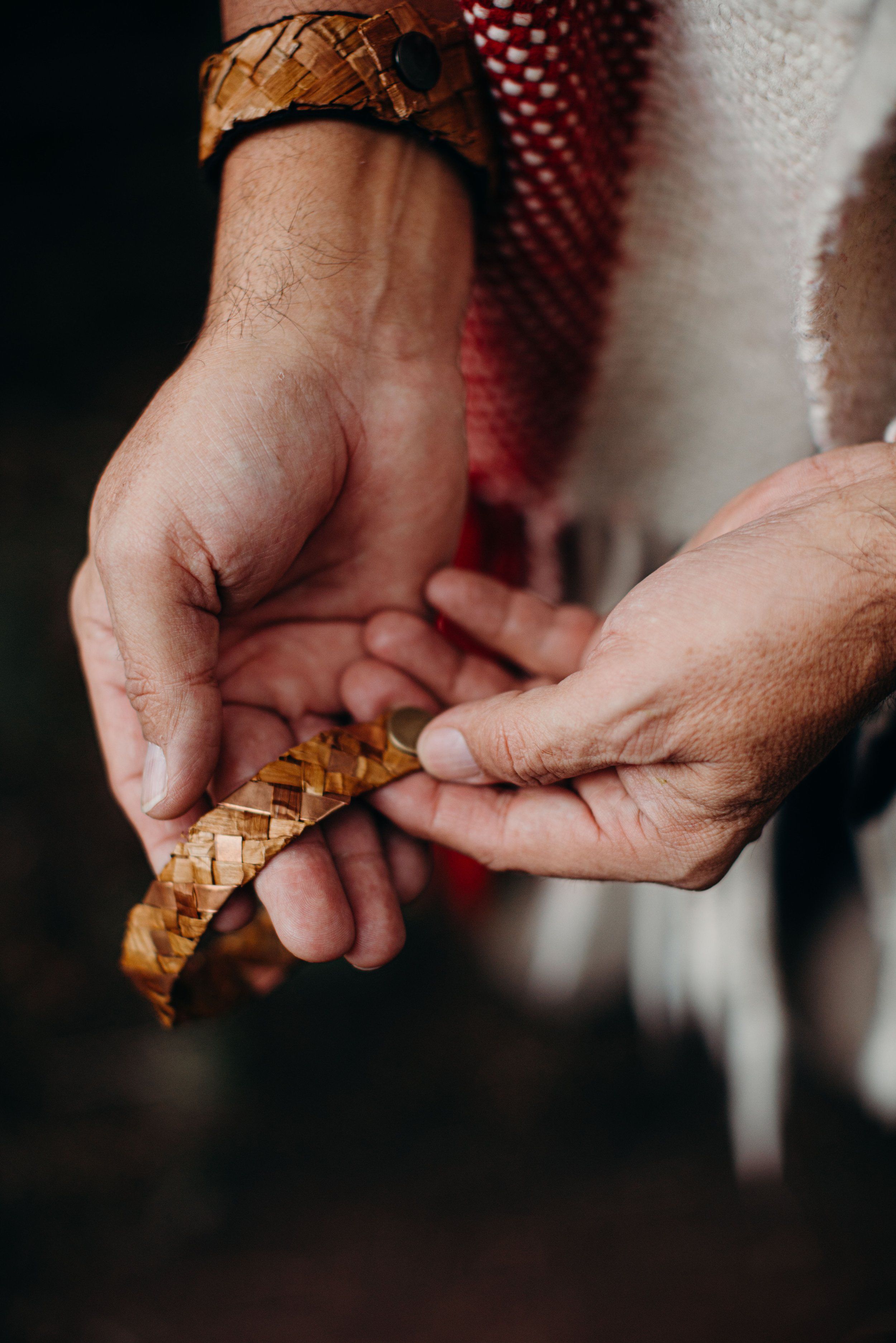 Two hands with earth-toned bracelets gently cradling a pine cone against dark fabric and natural lighting
