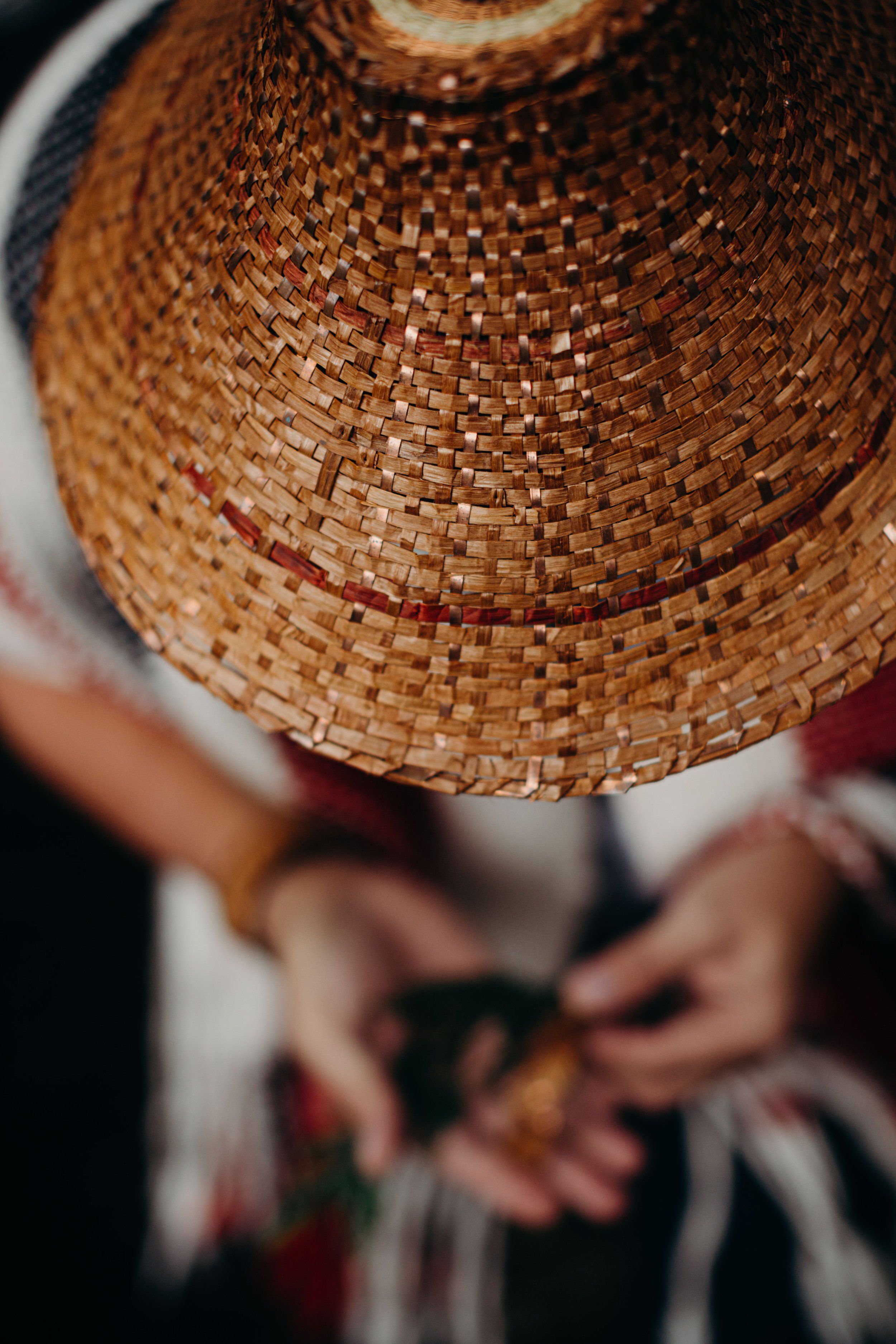 Hands holding a woven cone-shaped cedar hat against soft natural light, revealing intricate basket weave details