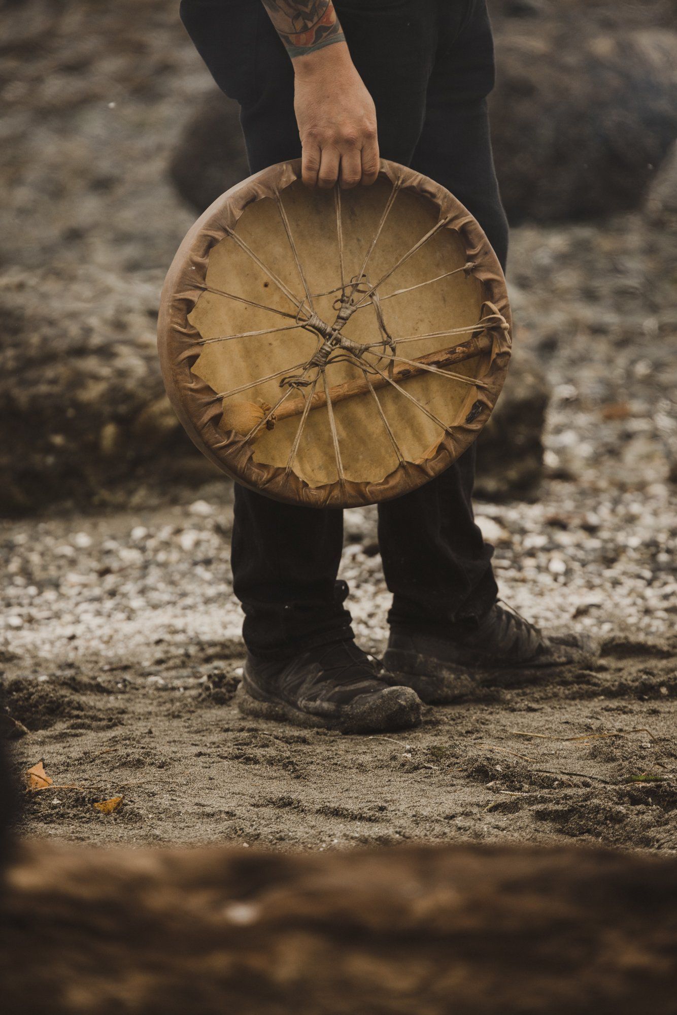 Person in dark clothing holds a weathered circular basket against earth-toned ground, intimate and contemplative