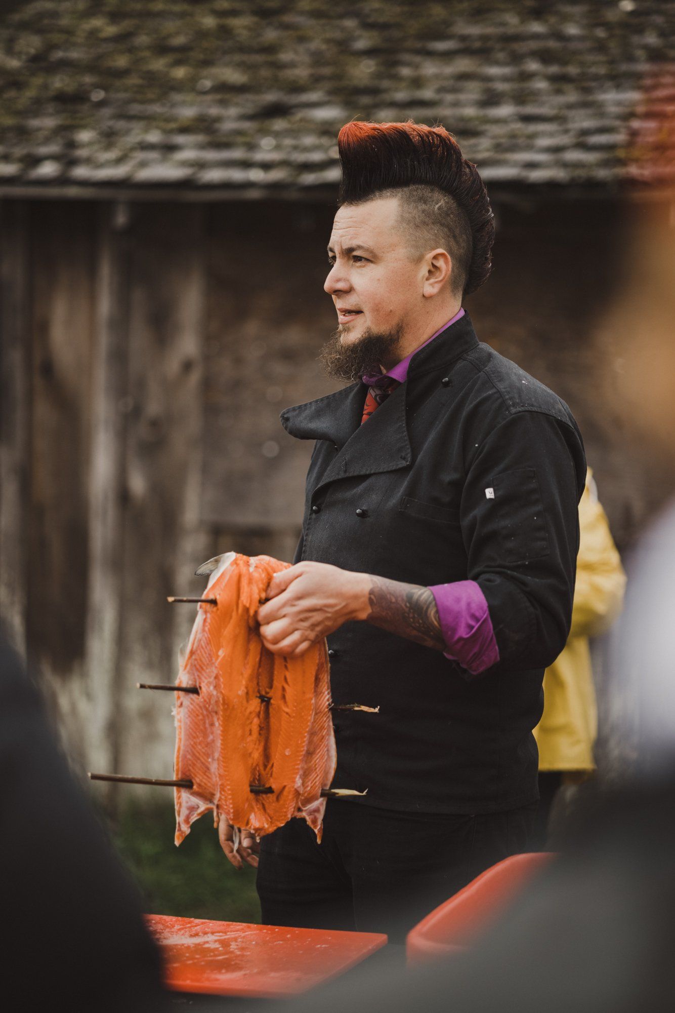 Man in black jacket holding orange-dyed fabric outdoors, warm sunlight illuminating textiles and traditional craft work