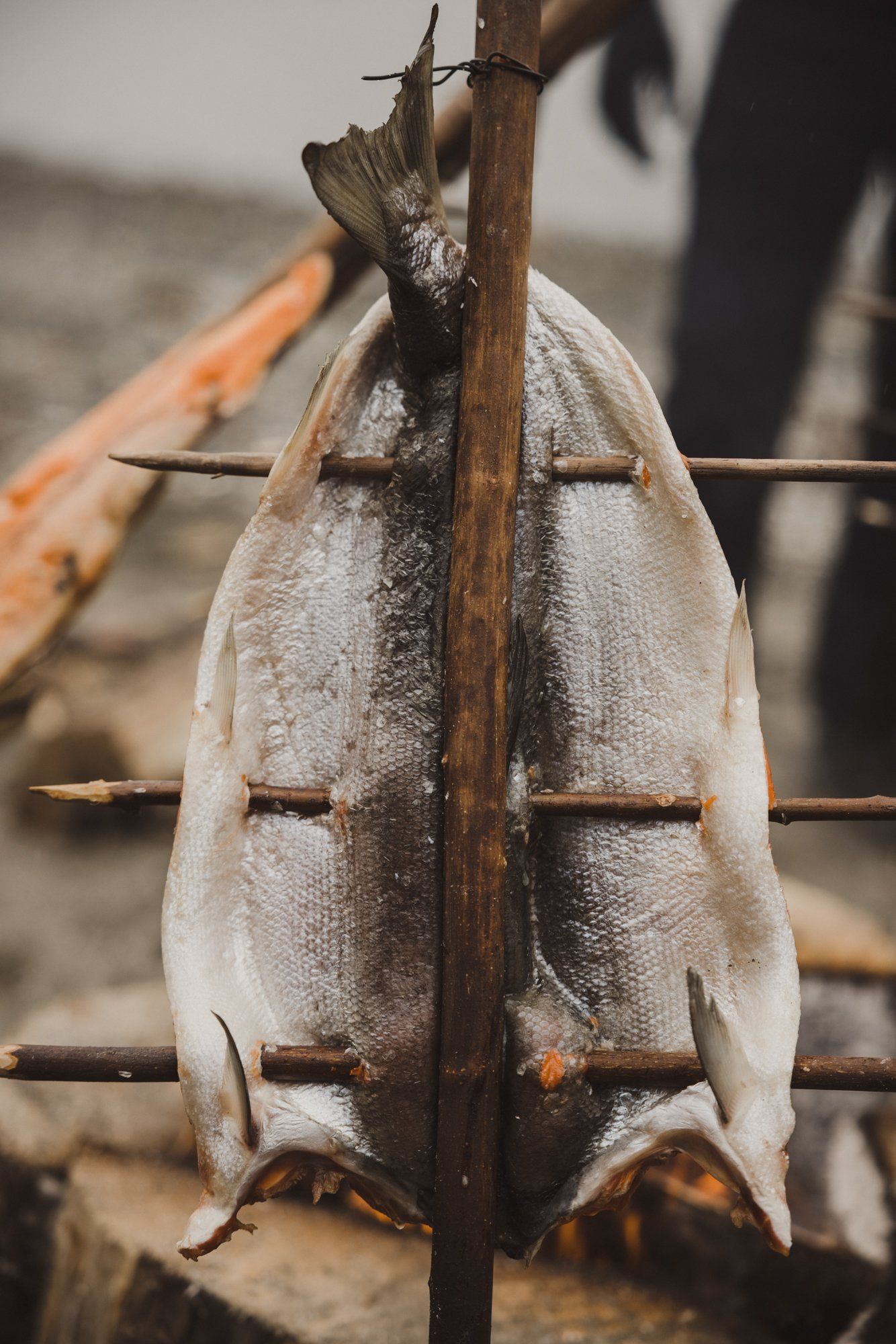 Fresh fish hung on wooden drying rack with ocean blurred in background
