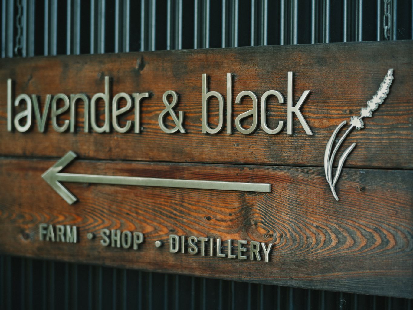 Weathered wood signage with metal letters reading "& blac" and "DISTILLERY" against corrugated metal backdrop