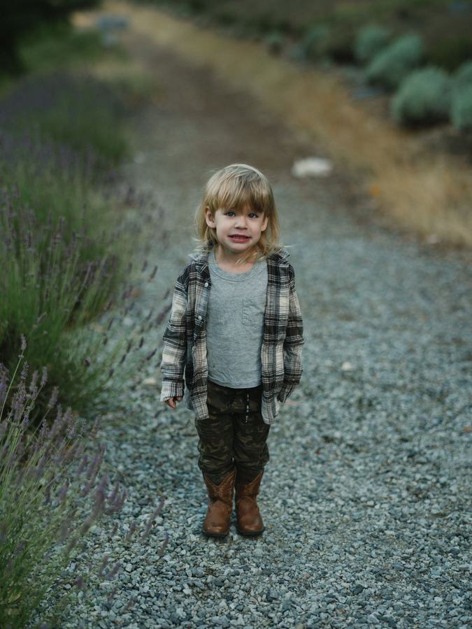 Blonde child in plaid shirt and boots on a gravel path at the lavender farm
