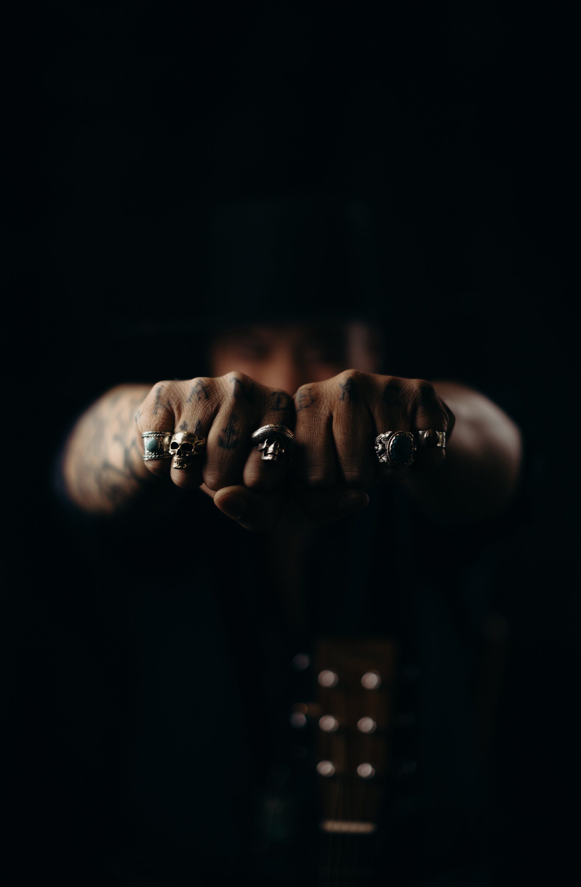 Hands with silver rings extended forward against dark background, dramatic side lighting illuminating skin tones and jewelry details
