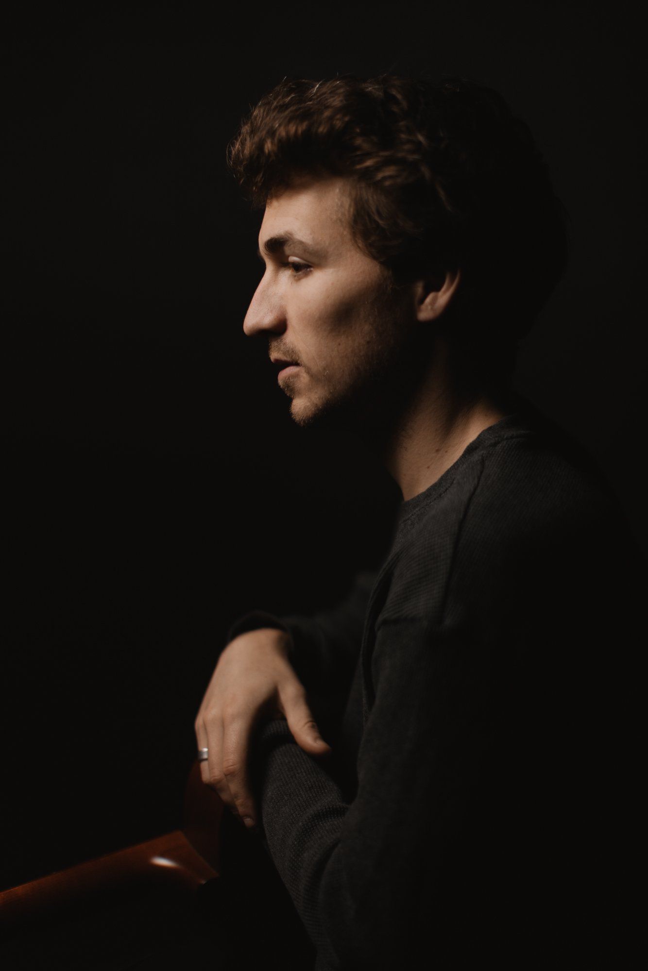 Profile portrait of man in black shirt against dark background, warm side lighting defining facial features and texture