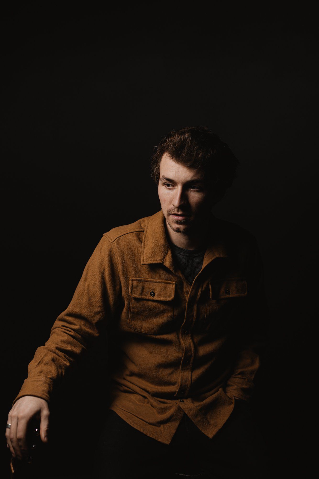 Man in warm-toned work shirt against dark background, posed with contemplative gaze and dramatic side lighting