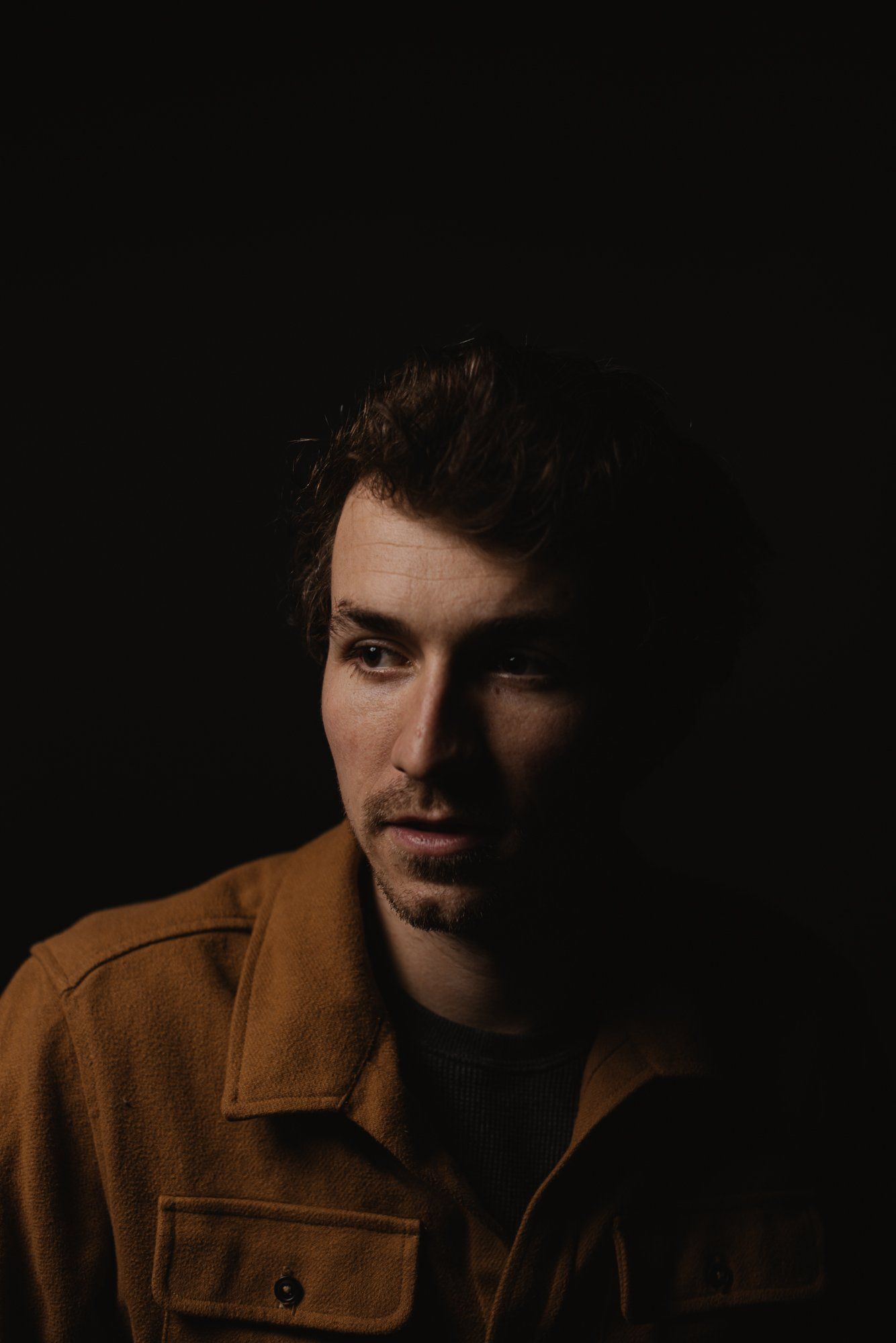 Man in mustard shirt against dark background, dramatic side lighting illuminating half his face
