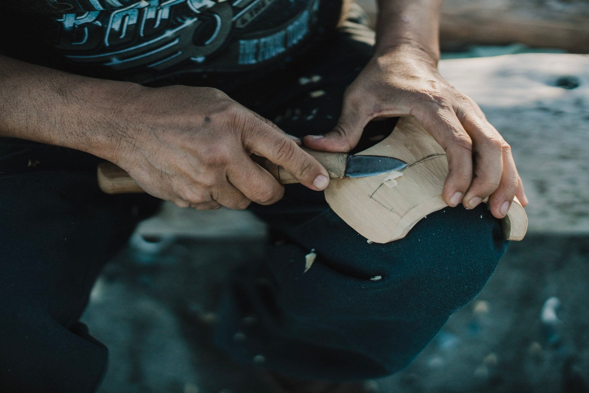 Hands carving intricate details into wood by the water, warm sunlight illuminating focused craftsmanship