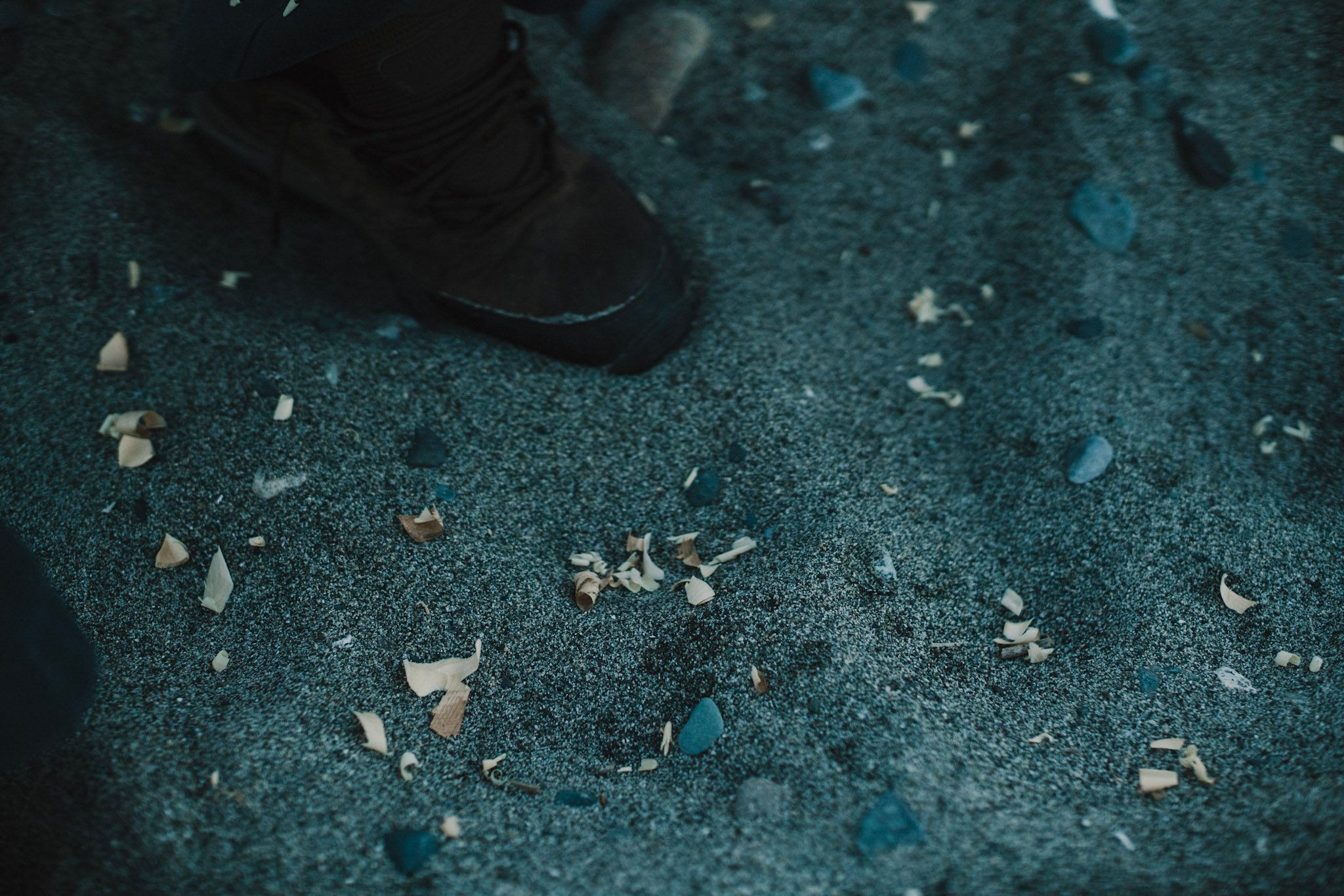 Boots standing on dark sand scattered with shells and pebbles, moody teal lighting