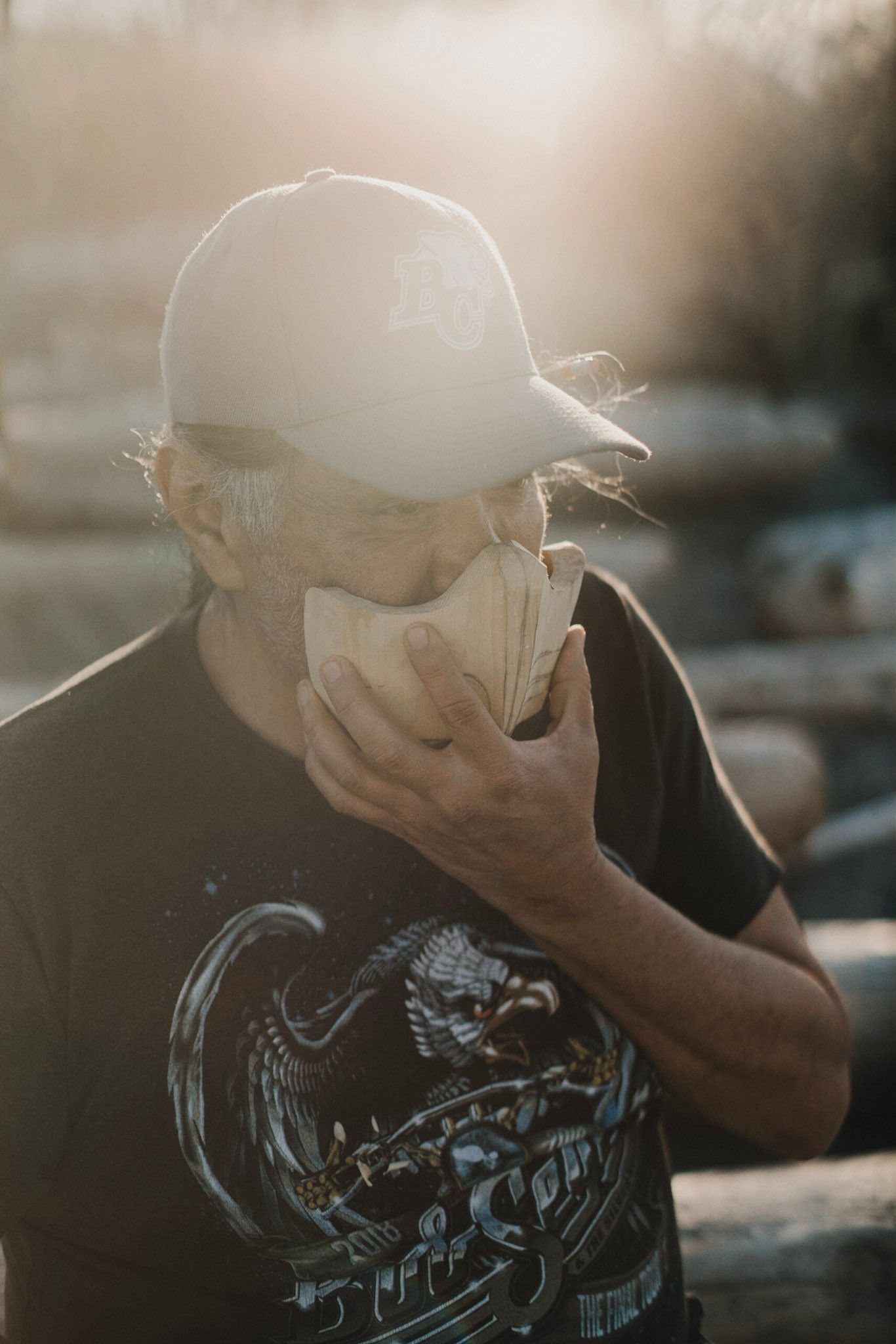 Man in graphic tee holds glowing orb before his face, backlit by golden afternoon light on a weathered rooftop