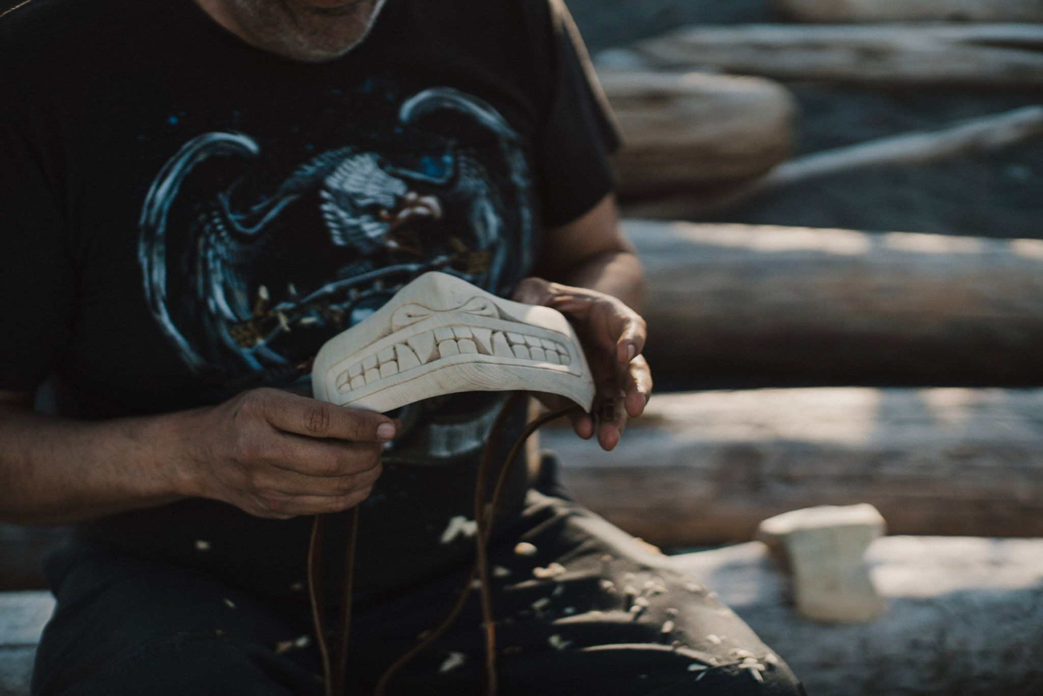 Hands holding a white canvas sneaker against weathered driftwood logs in natural sunlight
