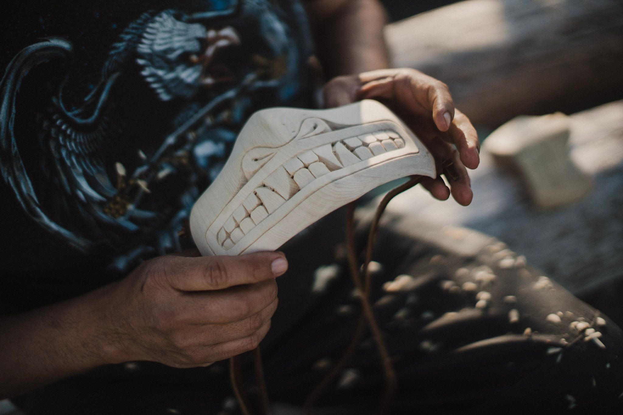 Hands holding a carved wooden shoe against sunlit stone, detail of artisan craftsmanship