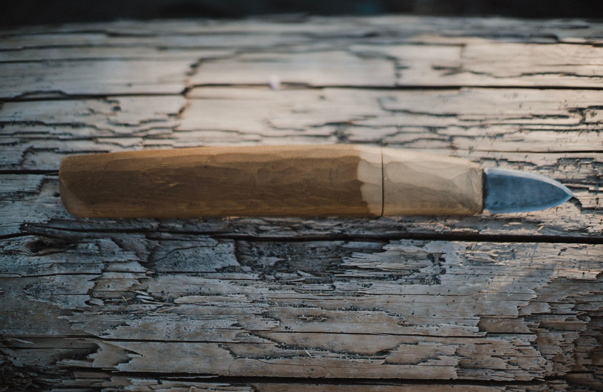 Weathered wooden carving tool with blue-painted tip resting on aged, cracked wood surface in natural light