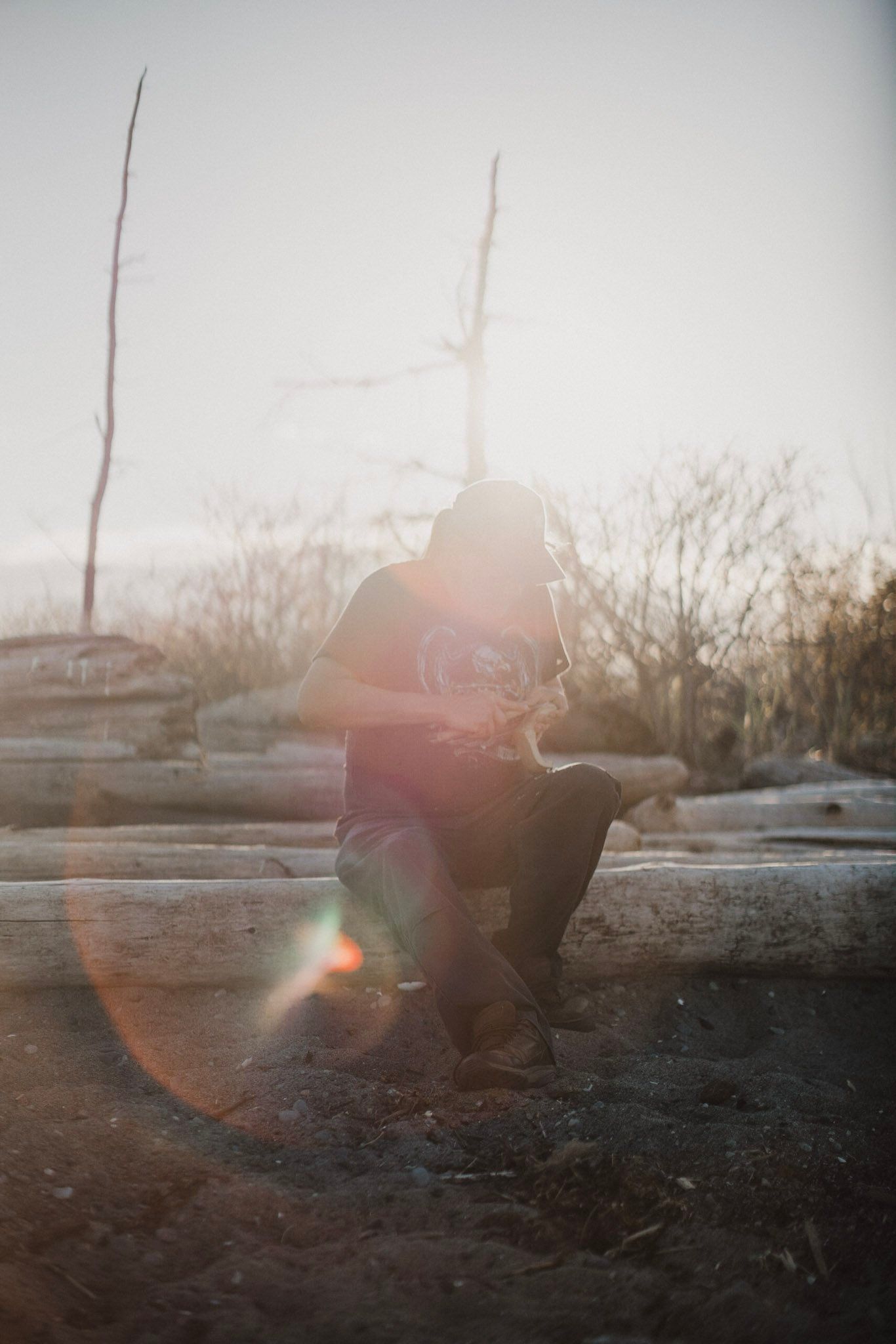 Man in warm light standing on misty waterfront with bare trees and sailboat behind him