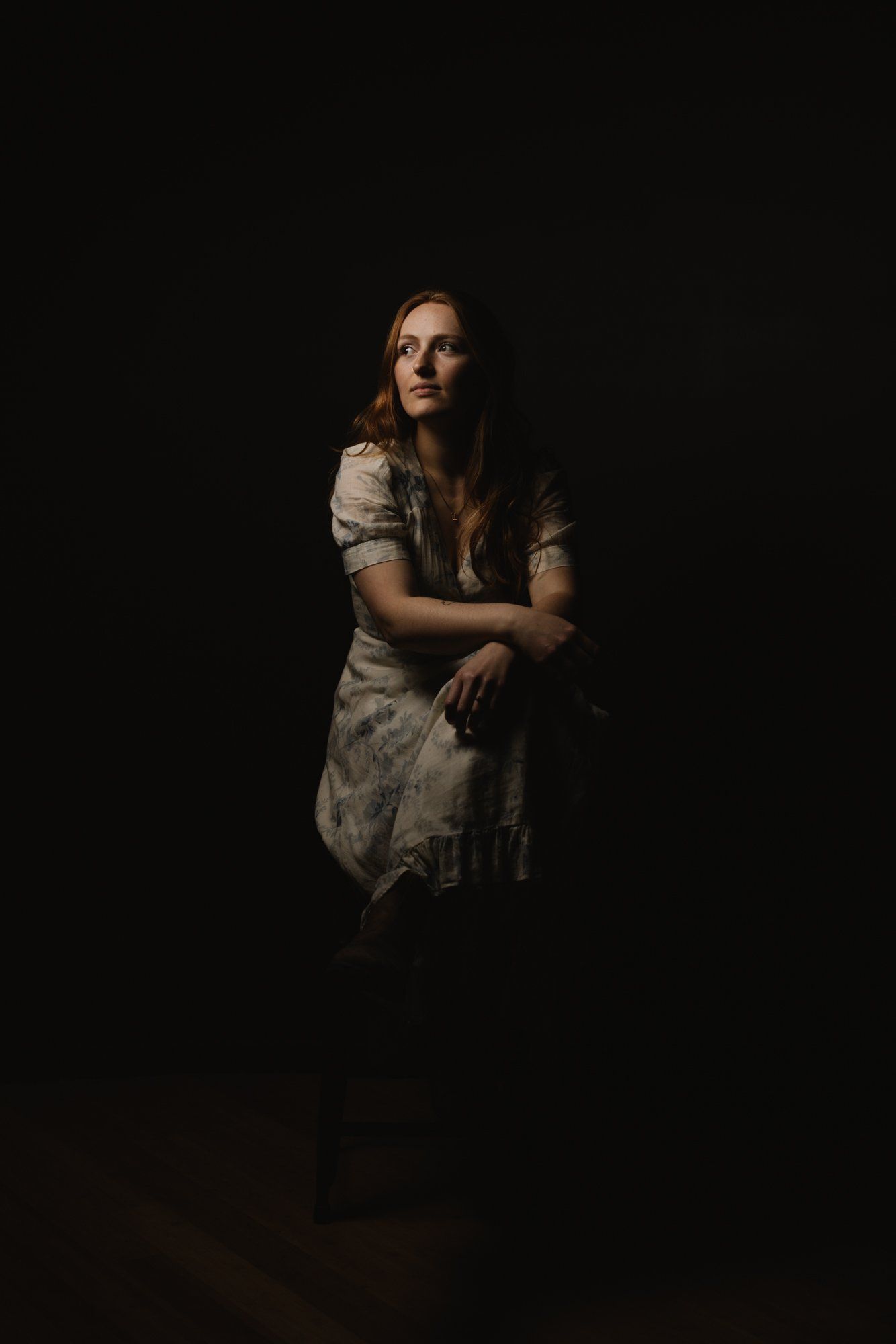 Woman in cream lace dress against dark background, gazing thoughtfully to the side with dramatic side lighting