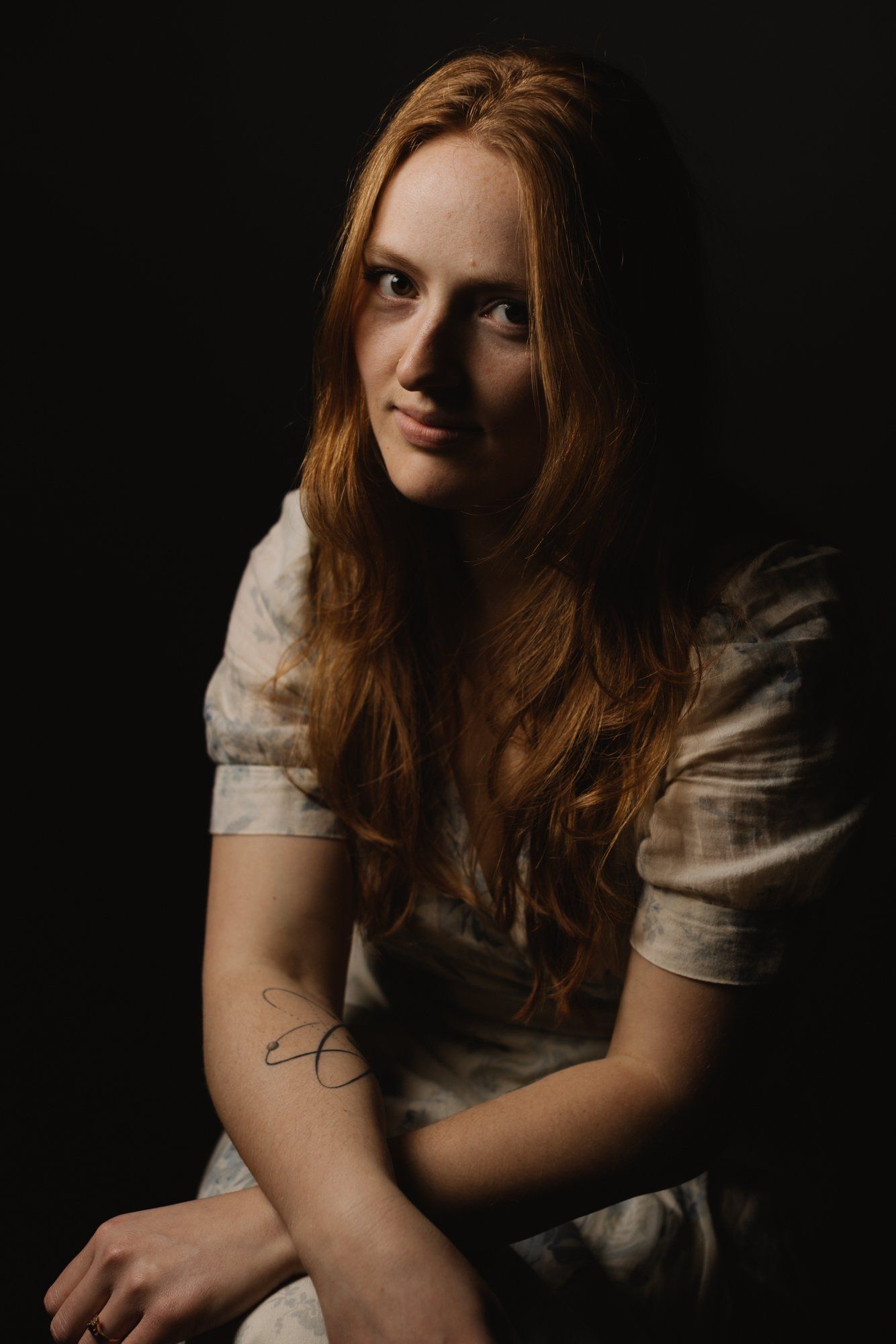 Woman with long reddish-brown hair in white shirt against dark background, soft dramatic lighting