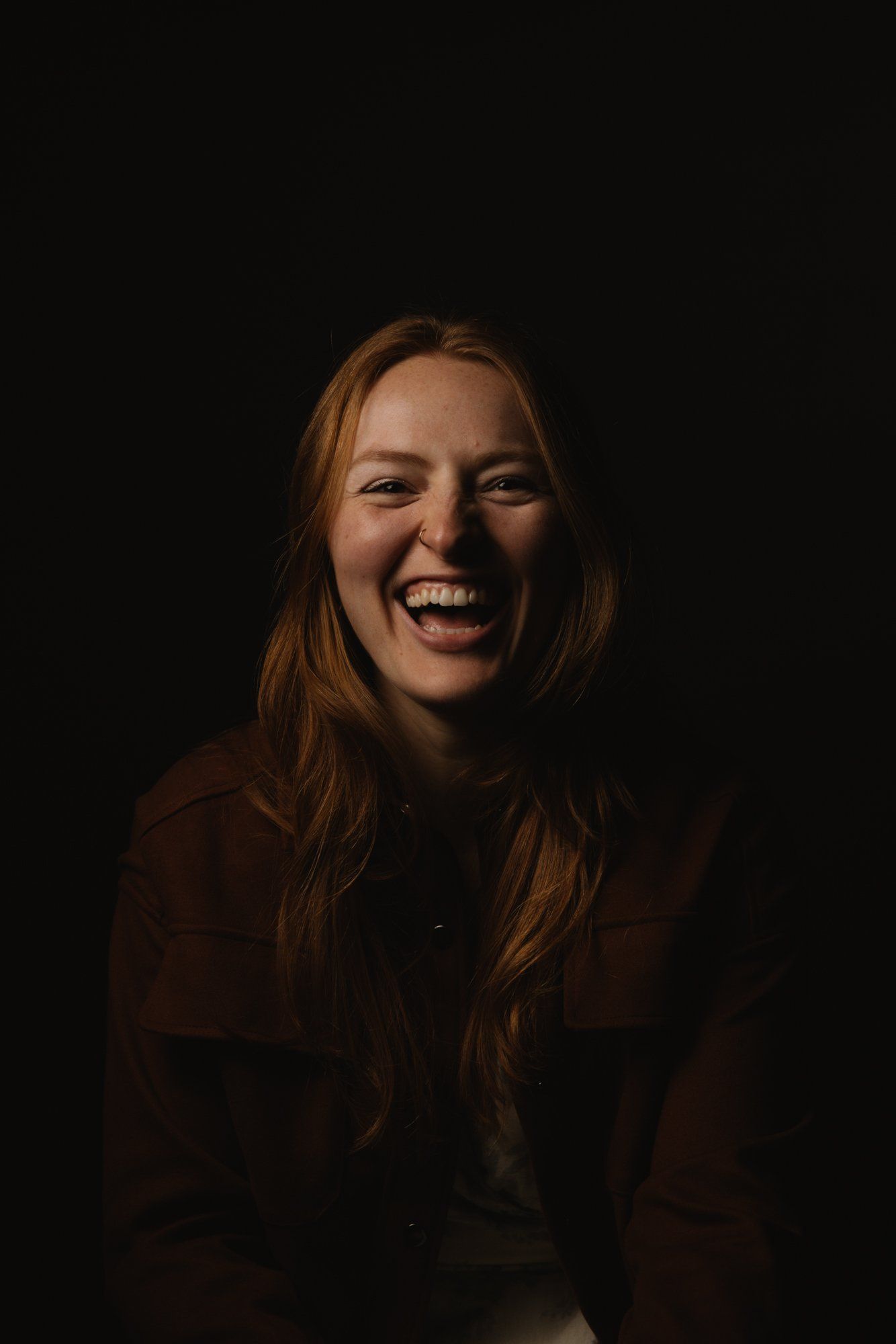 Woman with long auburn hair smiling warmly against dark background, lit by soft golden light from the side