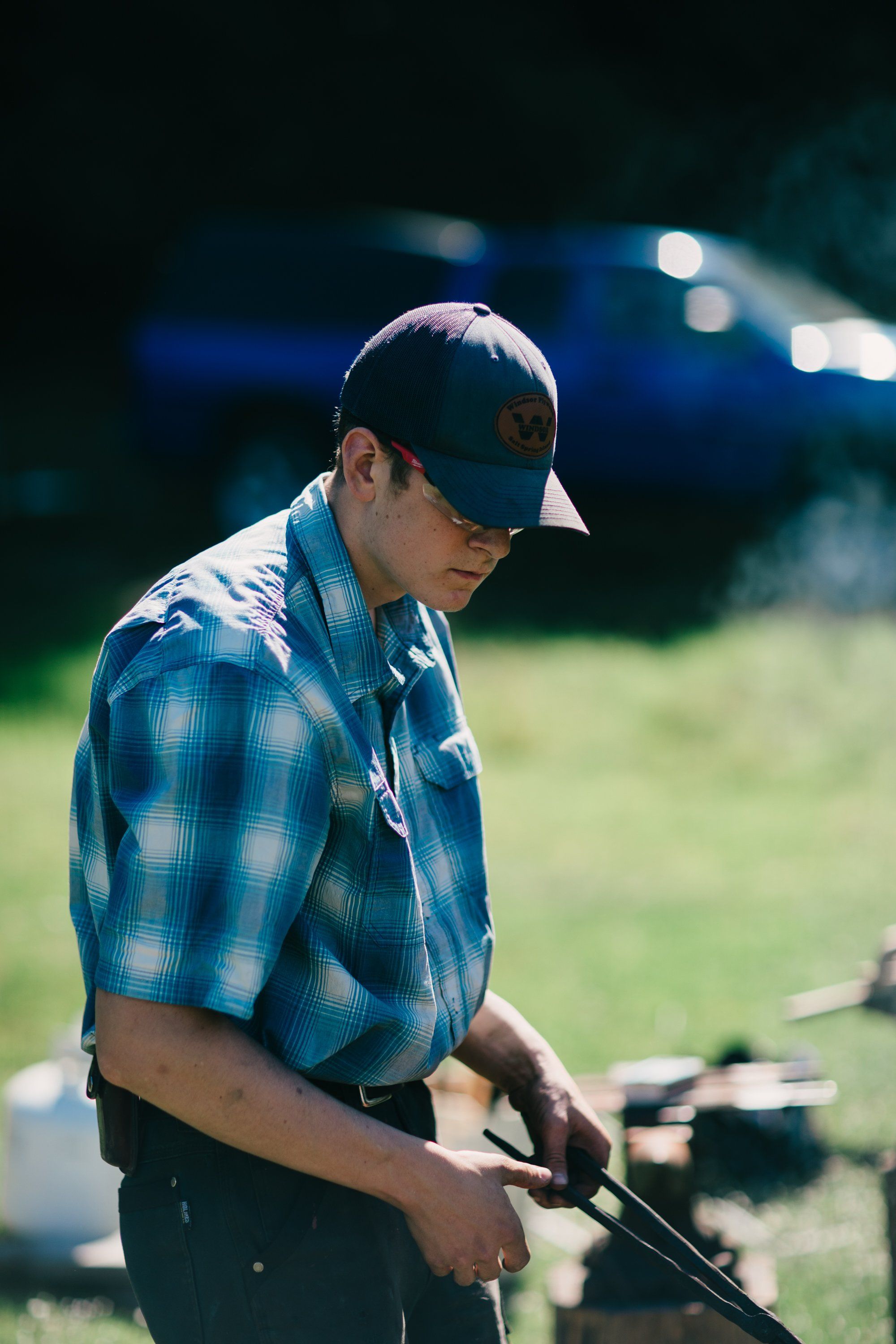 Young man in blue plaid shirt and cap working with tools at Ruckle Farm, golden afternoon light with blurred green fields behind