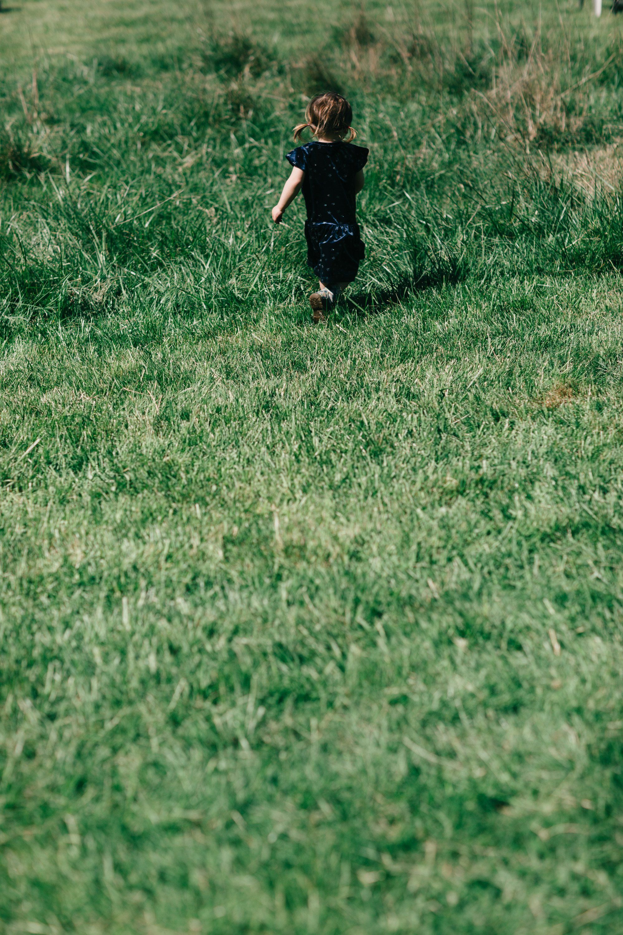 Child in dark clothing running through tall grass field on a sunny day