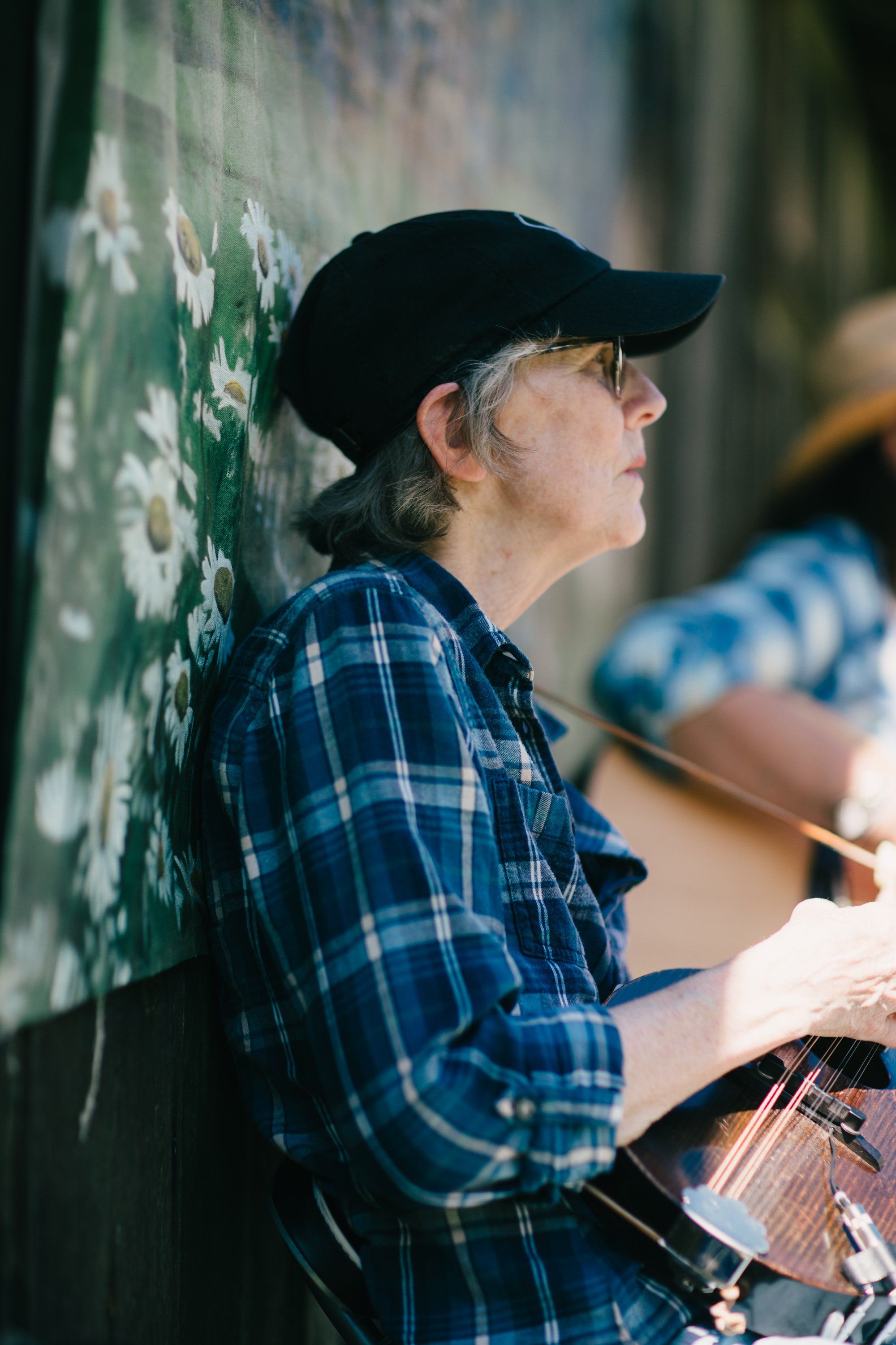 Artist in blue plaid shirt and black cap paints green mural on weathered wall at Ruckle Farm