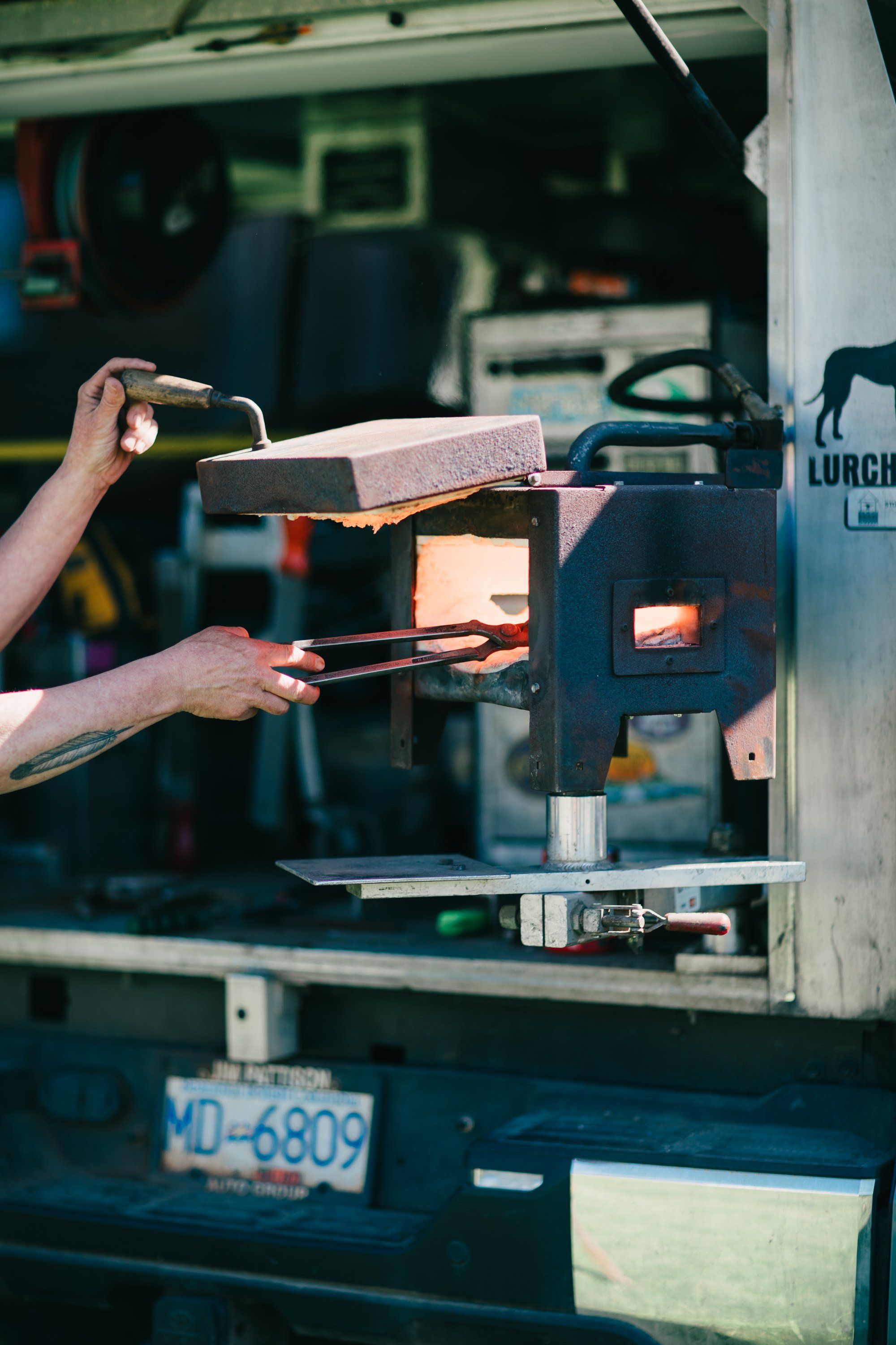 Blacksmith's hands guide glowing metal into a forge opening at Ruckle Farm, warm light illuminating traditional craftsmanship