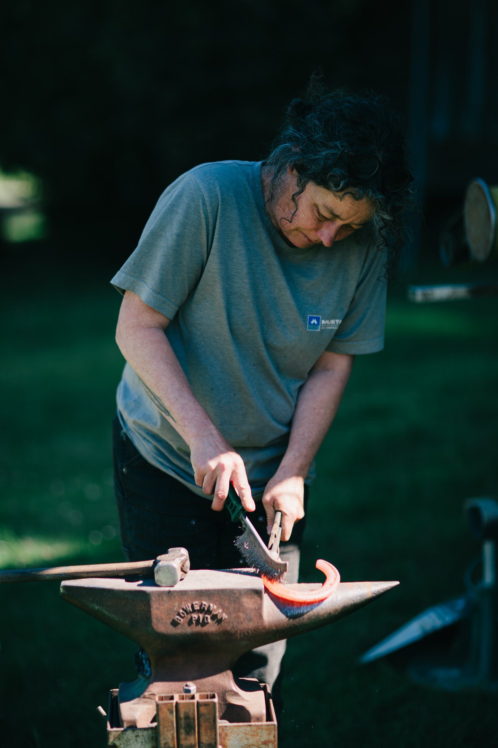 Blacksmith at anvil shaping metal with hammer and tongs, concentrated in dappled farm light