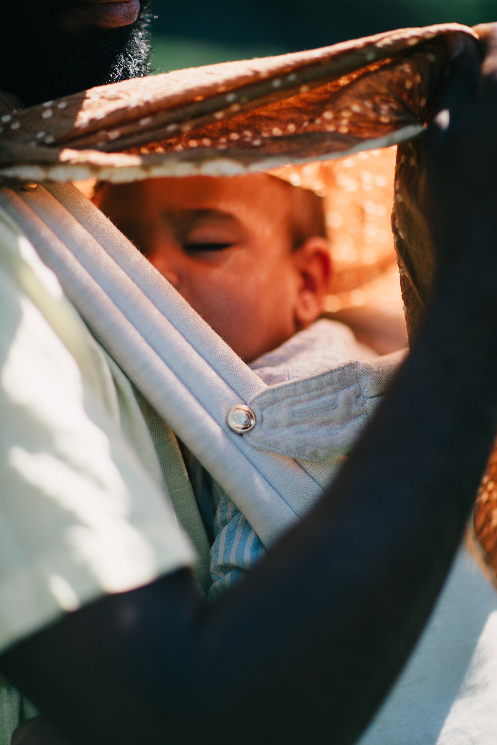 Child in striped shirt peering under wooden beam in warm afternoon light, eyes closed in gentle concentration