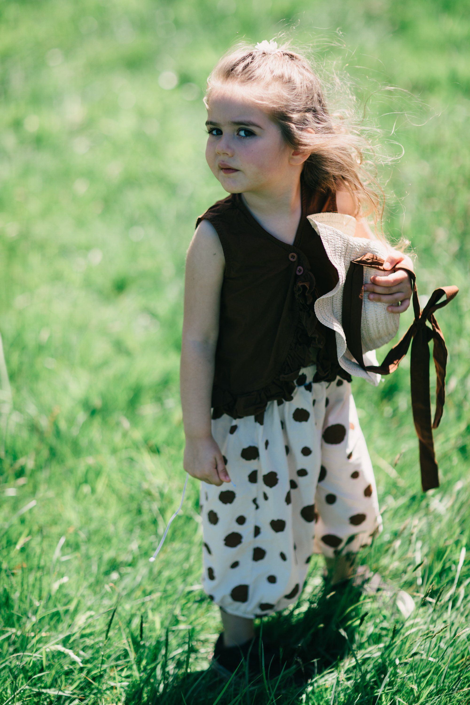 Young girl in polka-dot skirt holding wildflowers in a sunlit meadow at Ruckle Farm