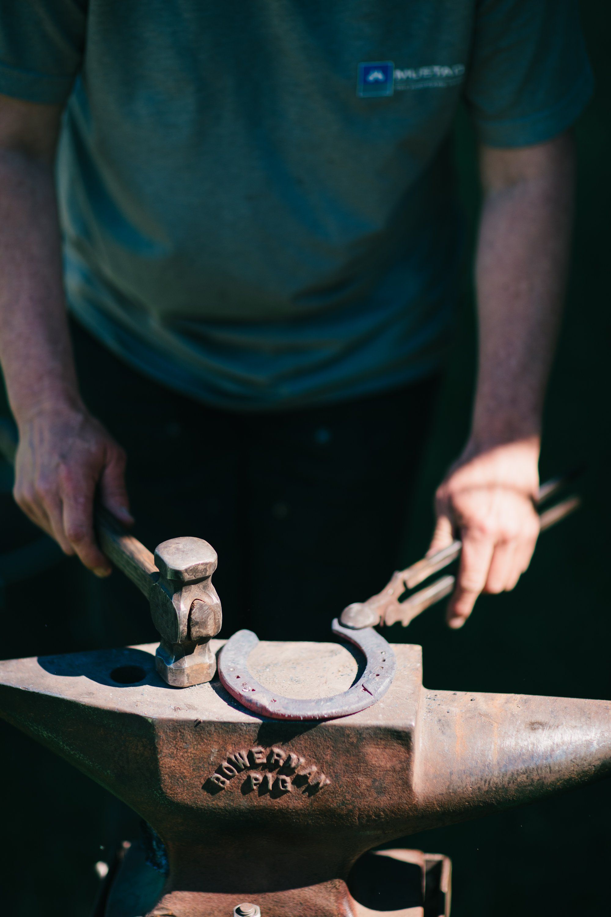 Blacksmith's hands holding hammer and tongs above a glowing horseshoe on an anvil, warm light casting shadows in a working forge