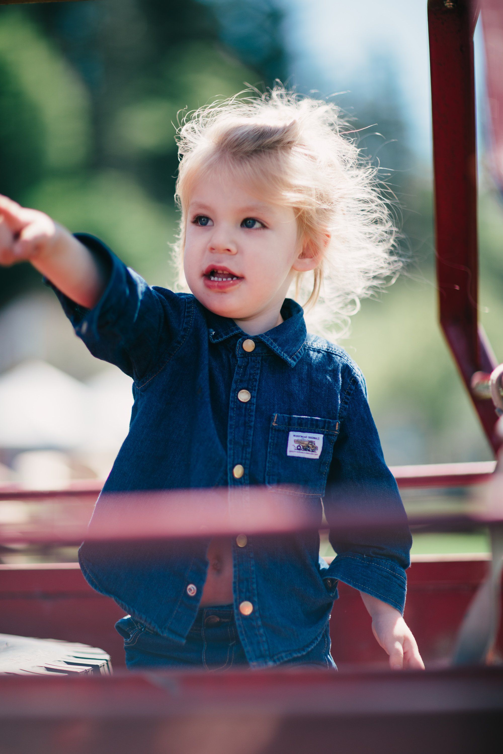 Toddler in denim jacket reaches toward red farm equipment in golden afternoon light at Ruckle Farm