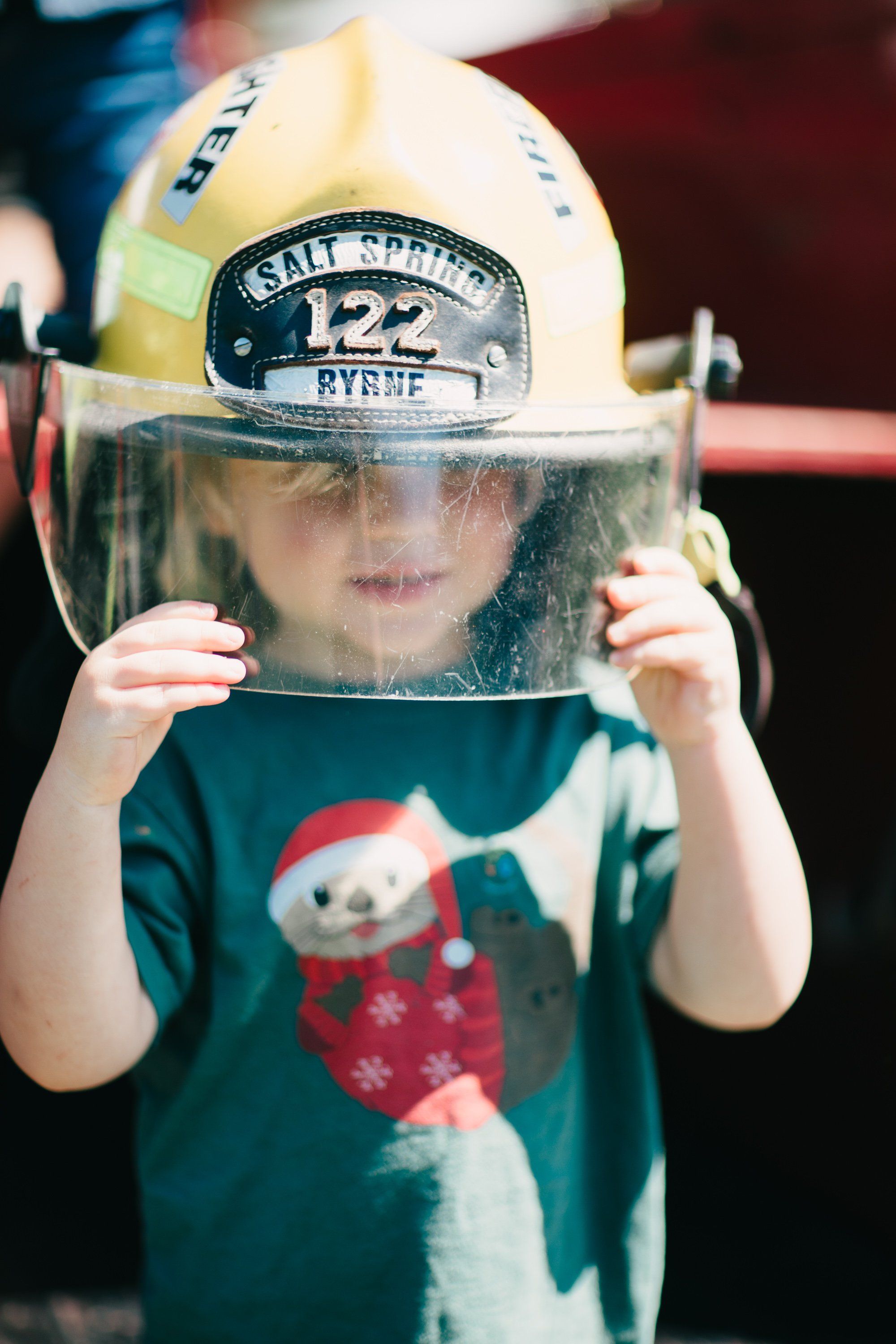 Child in festive sweater peers through firefighter helmet with clear visor at Ruckle Farm
