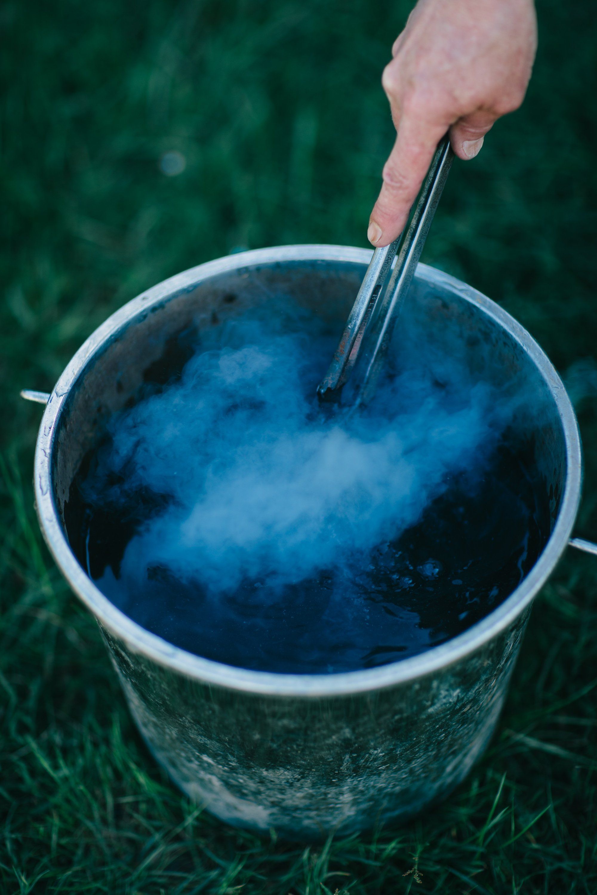 Hand stirring a bucket of deep indigo dye against verdant grass at Ruckle Farm