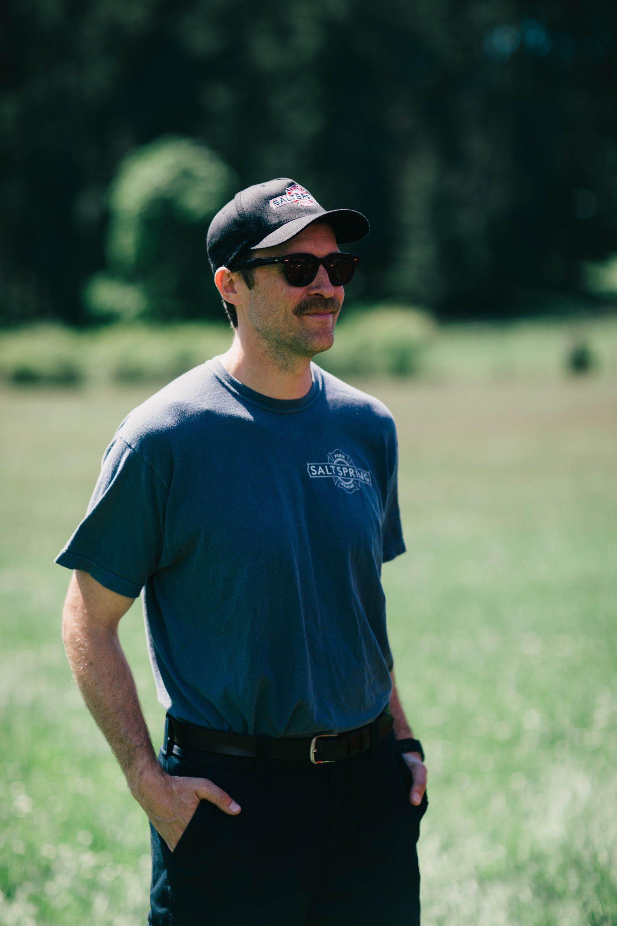 Man in navy shirt and cap standing in open field with forested background, golden afternoon light