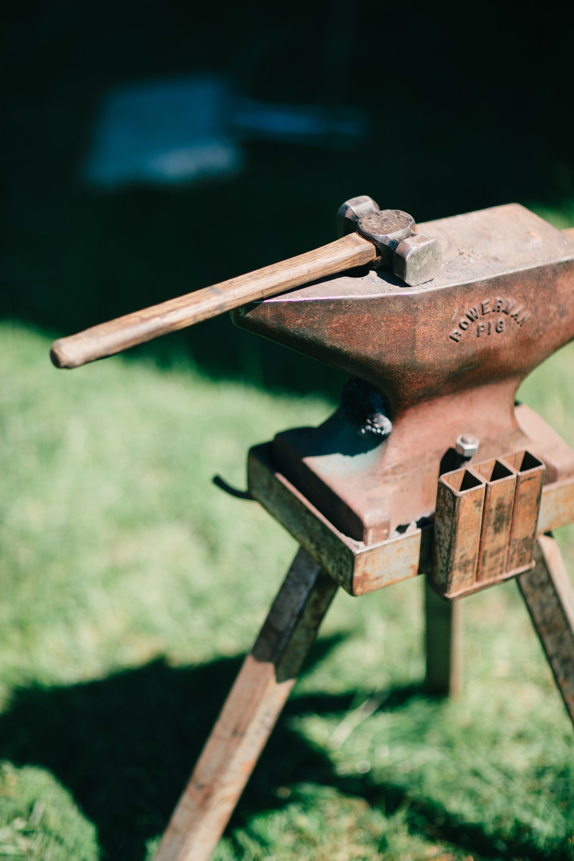 Weathered anvil and hammer on tripod stand with green grass and blue water blurred in background