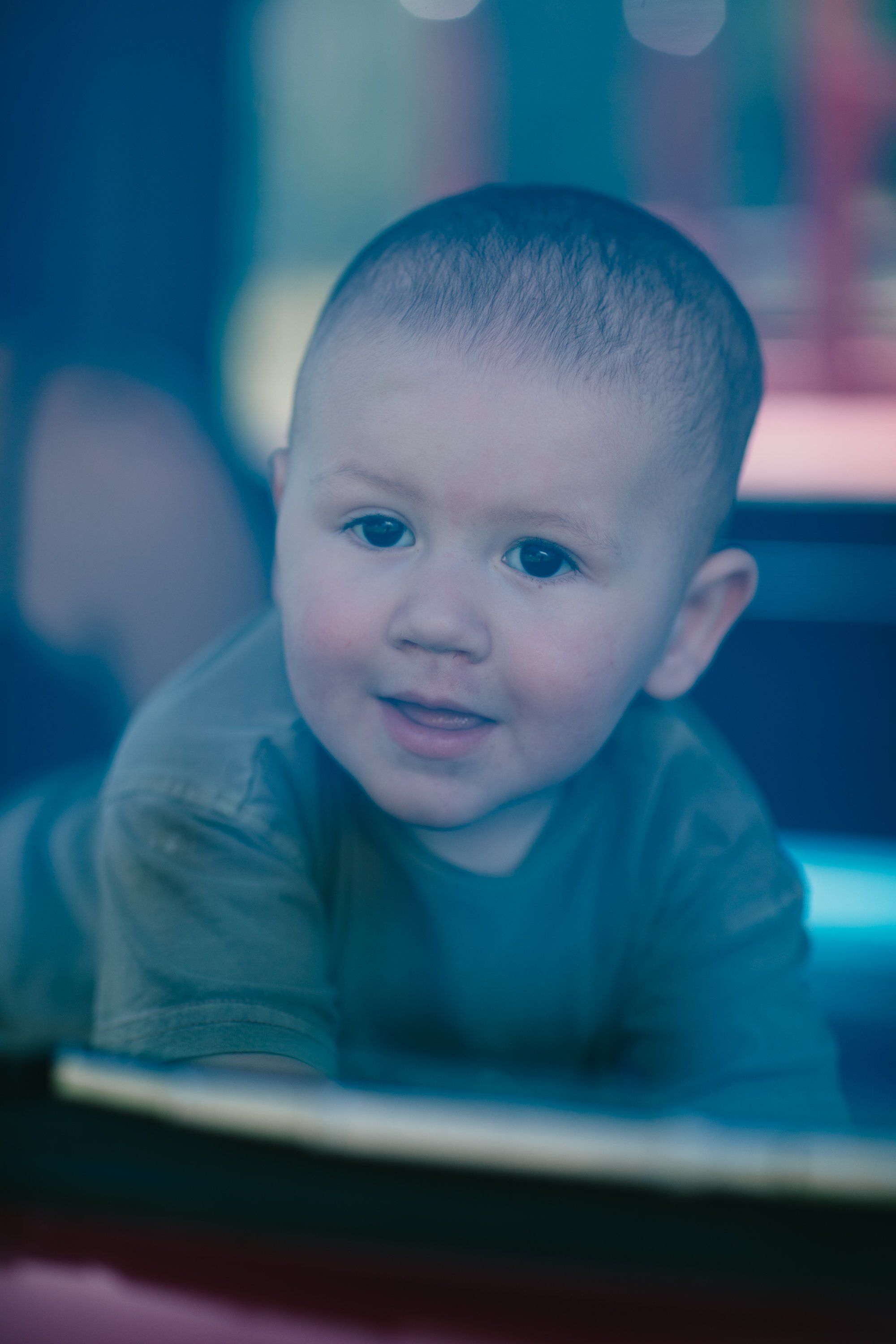 Toddler with bright eyes gazes directly at camera, soft blue and pink bokeh light diffusing behind him