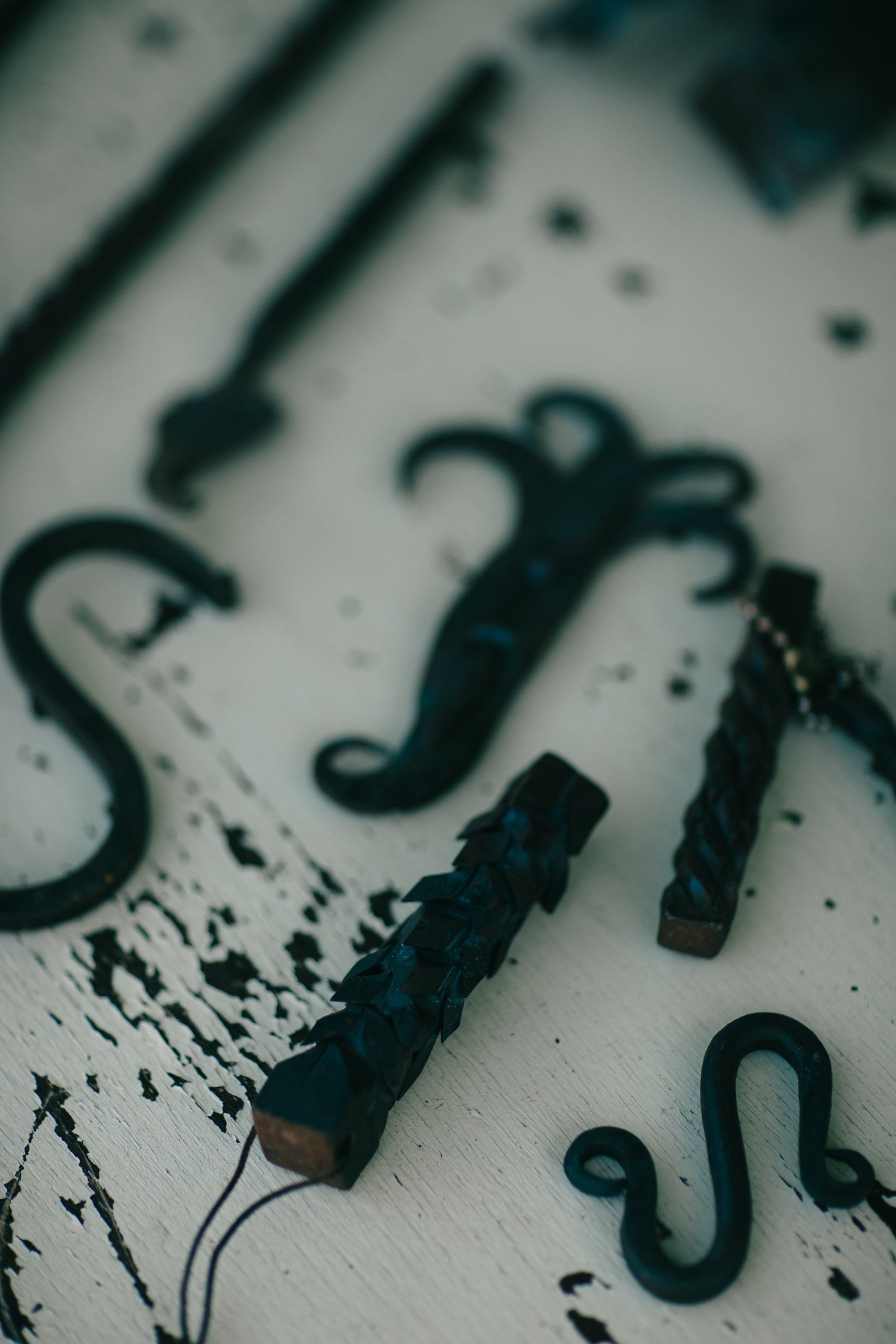 Weathered farm tools with S-hooks and handles arranged on a distressed white surface, casting soft shadows in natural light