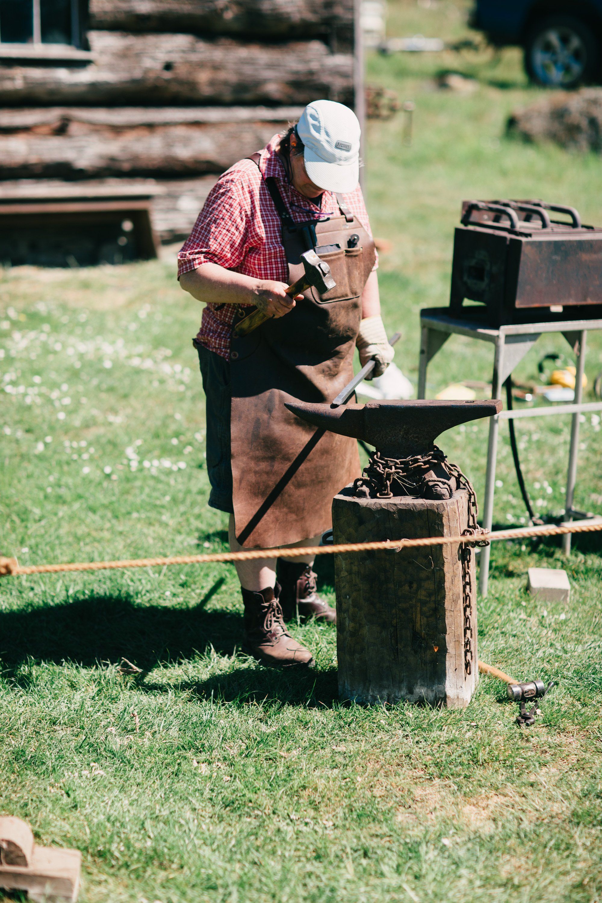Man in plaid shirt and white cap working at wooden workbench in sunlit farmyard setting