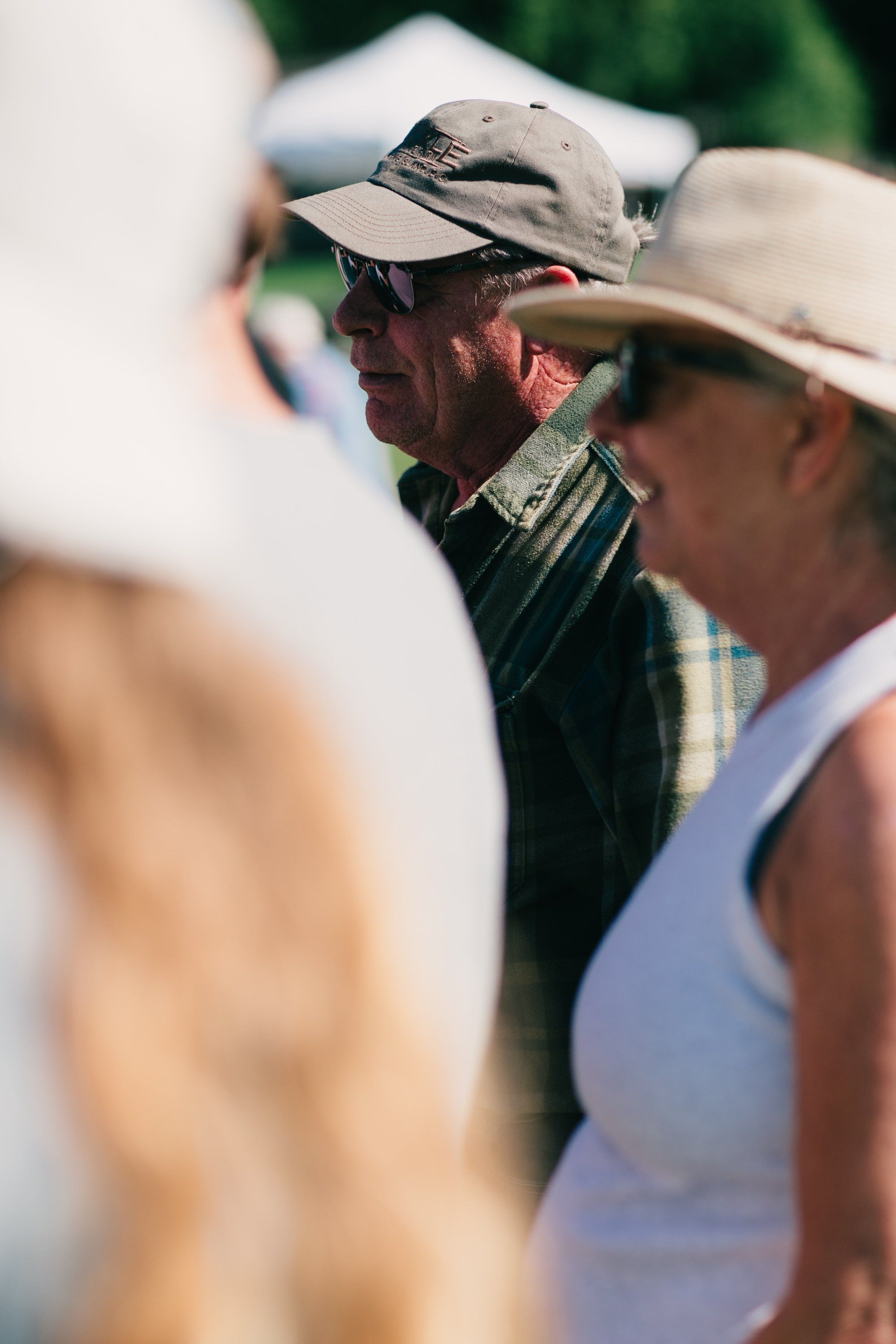 Farmer in weathered hat and work shirt converses with woman in white tank top under bright summer sunlight at Ruckle Farm